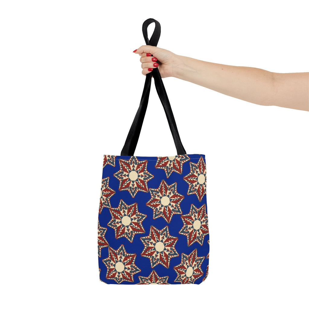 Blue tote bag with starburst floral mandala pattern and black handles, hanging view