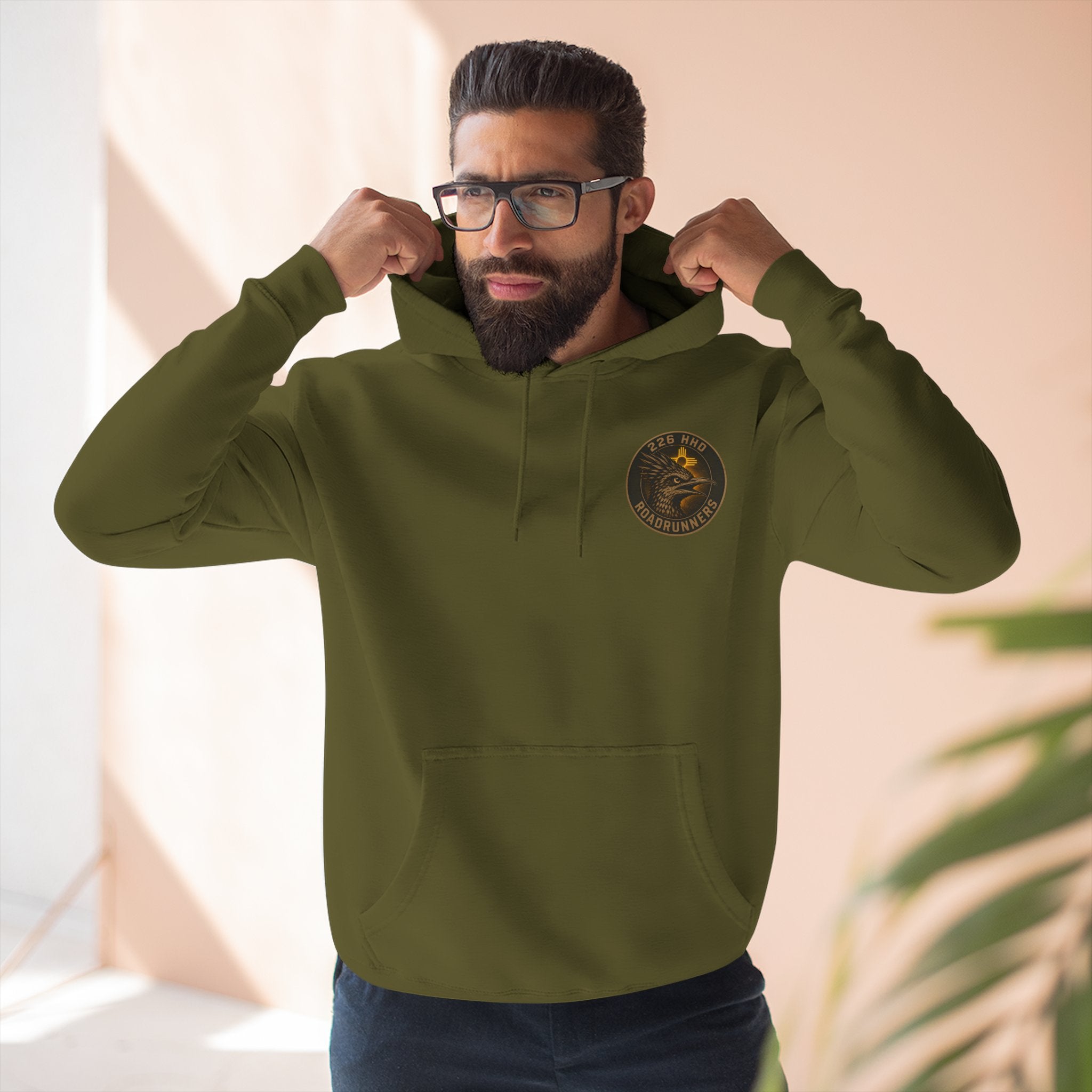 Army green cotton pullover hoodie with kangaroo pocket and chest emblem, worn.