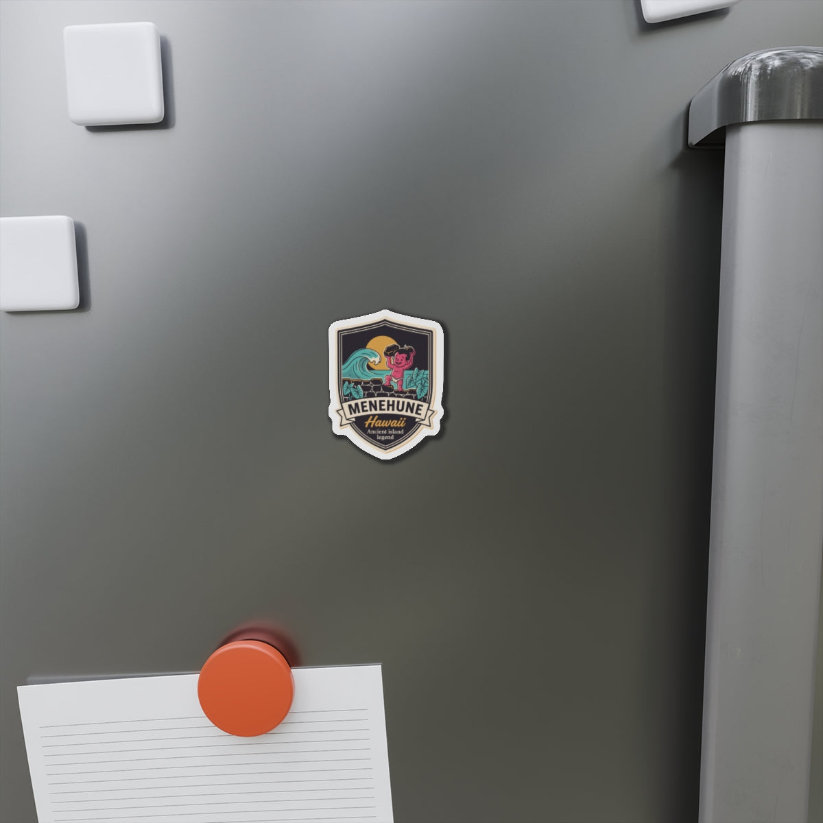 Small shield die-cut magnet on a metal surface, showing teal wave, pink character, and “Menehune Hawaii”