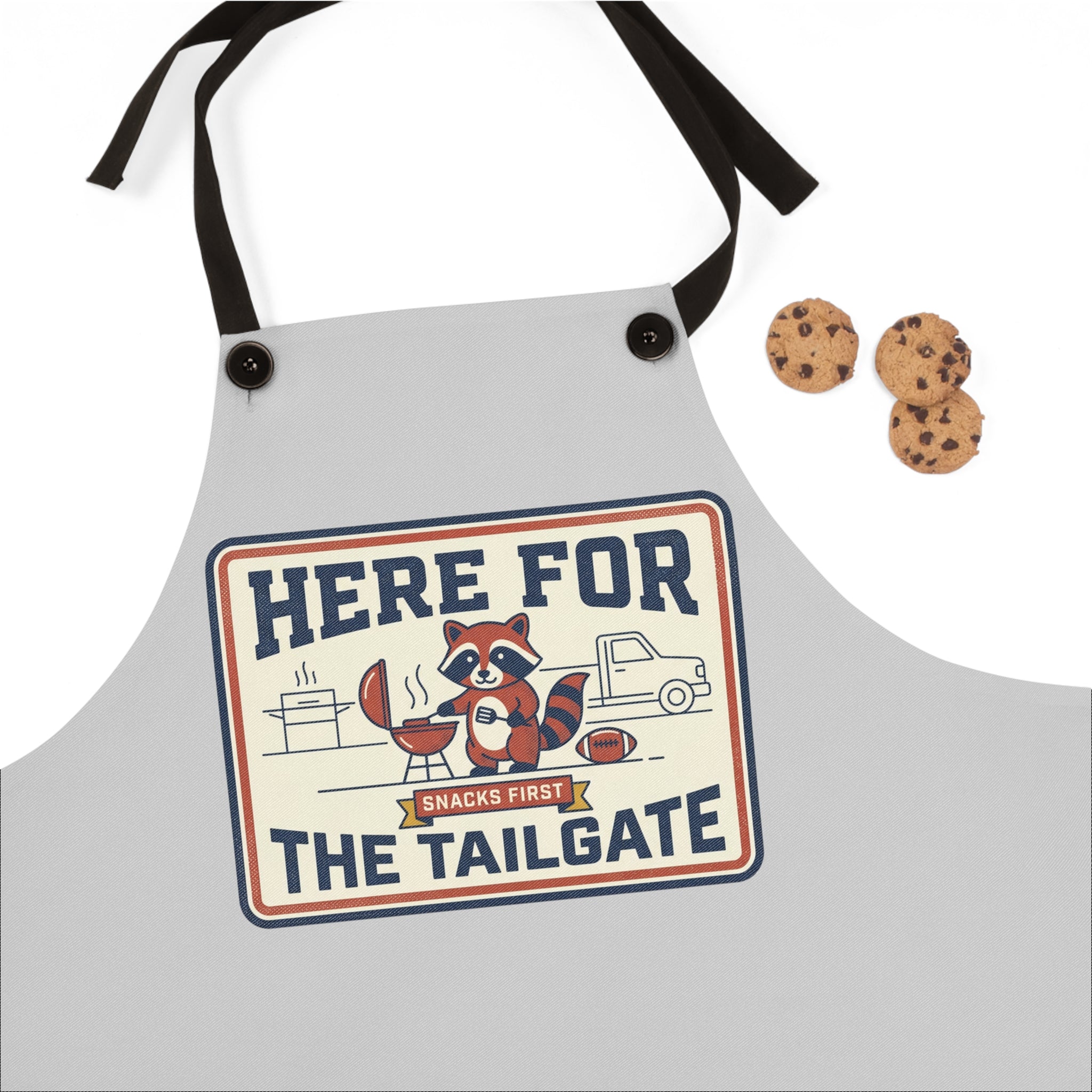 Light gray apron close-up: 'HERE FOR THE TAILGATE' print with raccoon BBQ cartoon