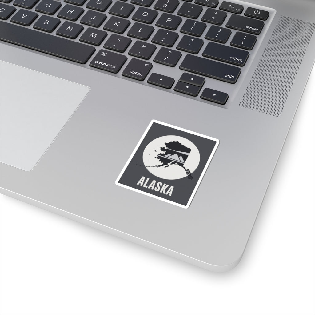 Square Alaska sticker with mountain silhouette and 'ALASKA' text on dark laptop