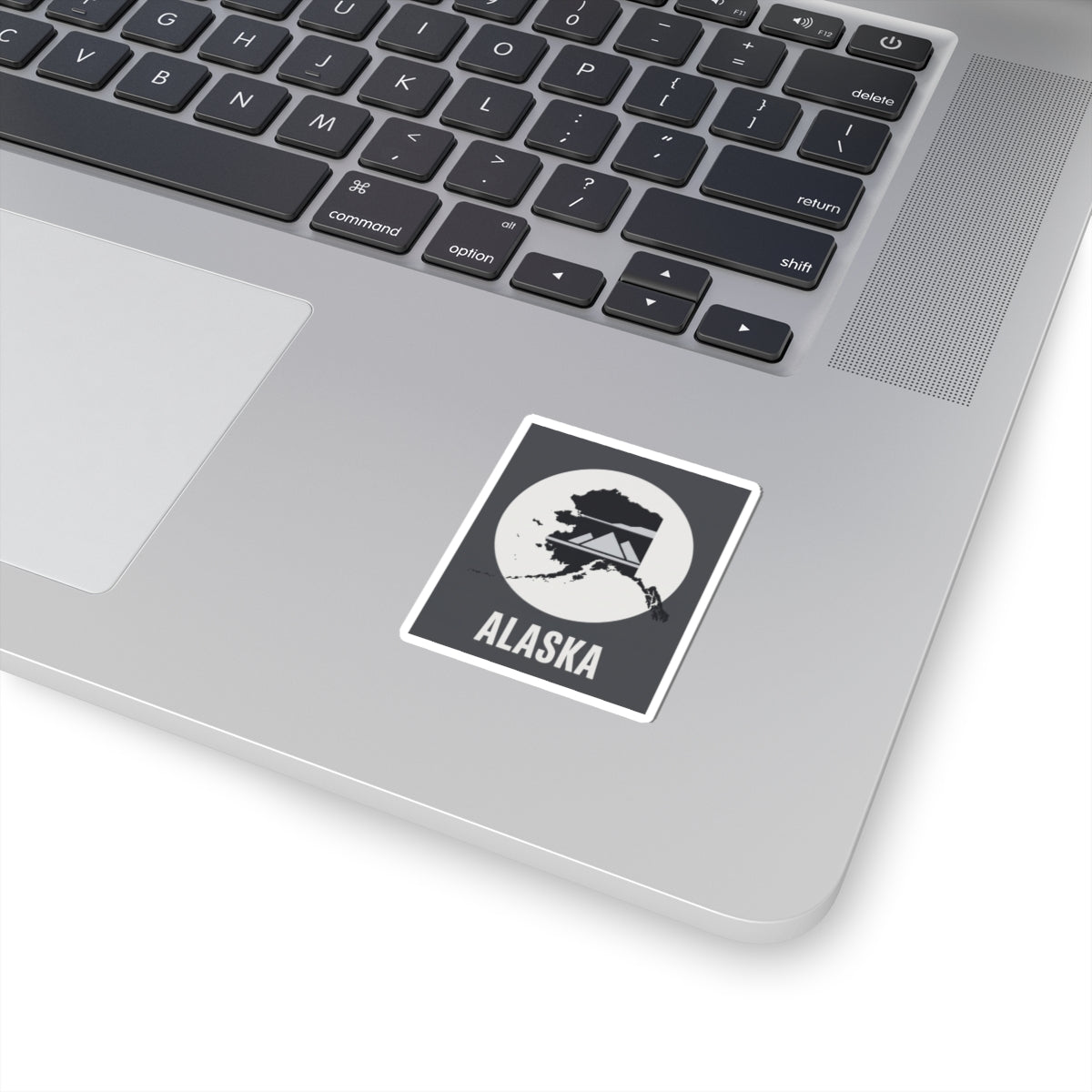 Square Alaska sticker with mountain silhouette and 'ALASKA' text on dark laptop