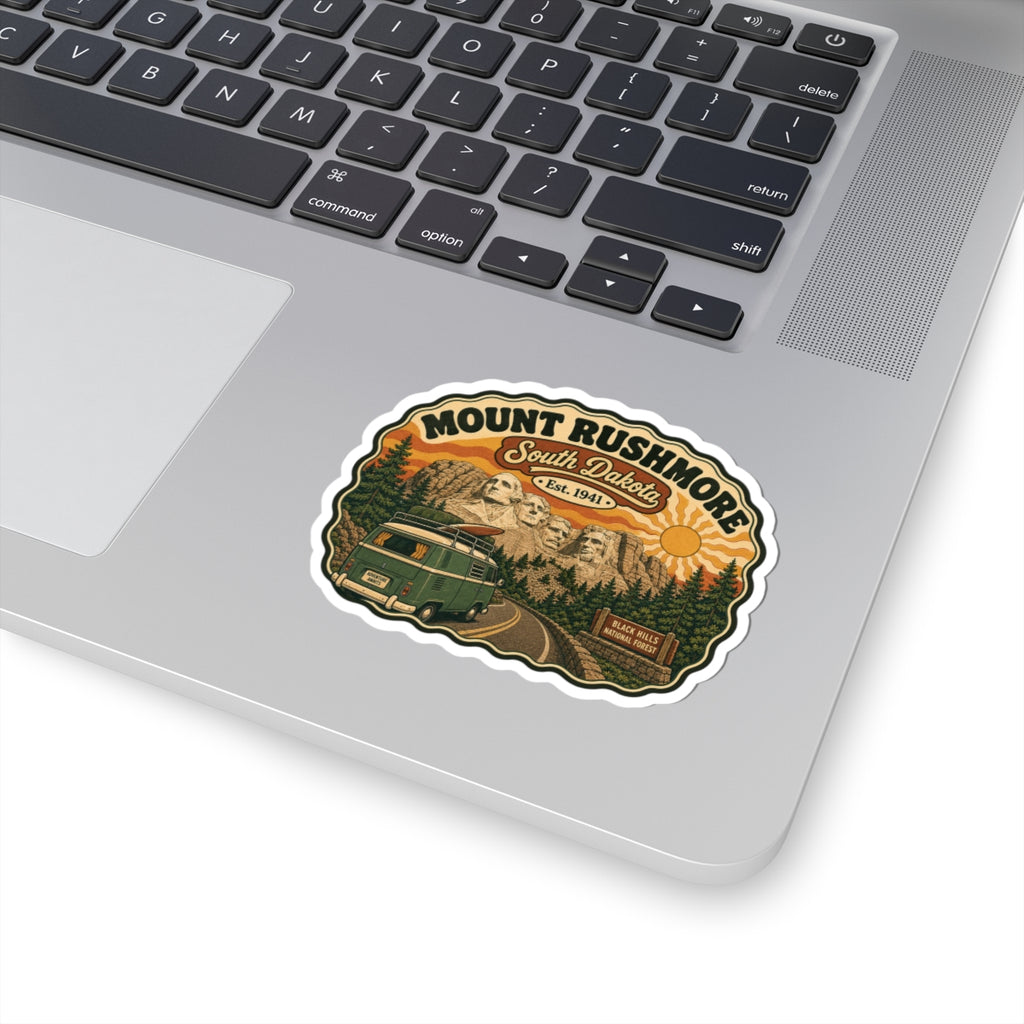Die-cut sticker on laptop lid, showing Mount Rushmore, South Dakota, and green camper