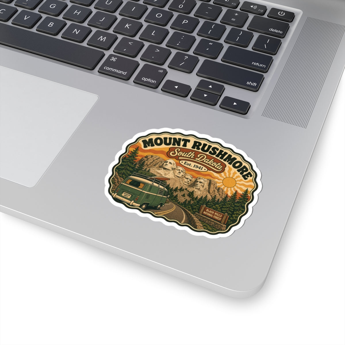 Die-cut sticker on laptop lid, showing Mount Rushmore, South Dakota, and green camper