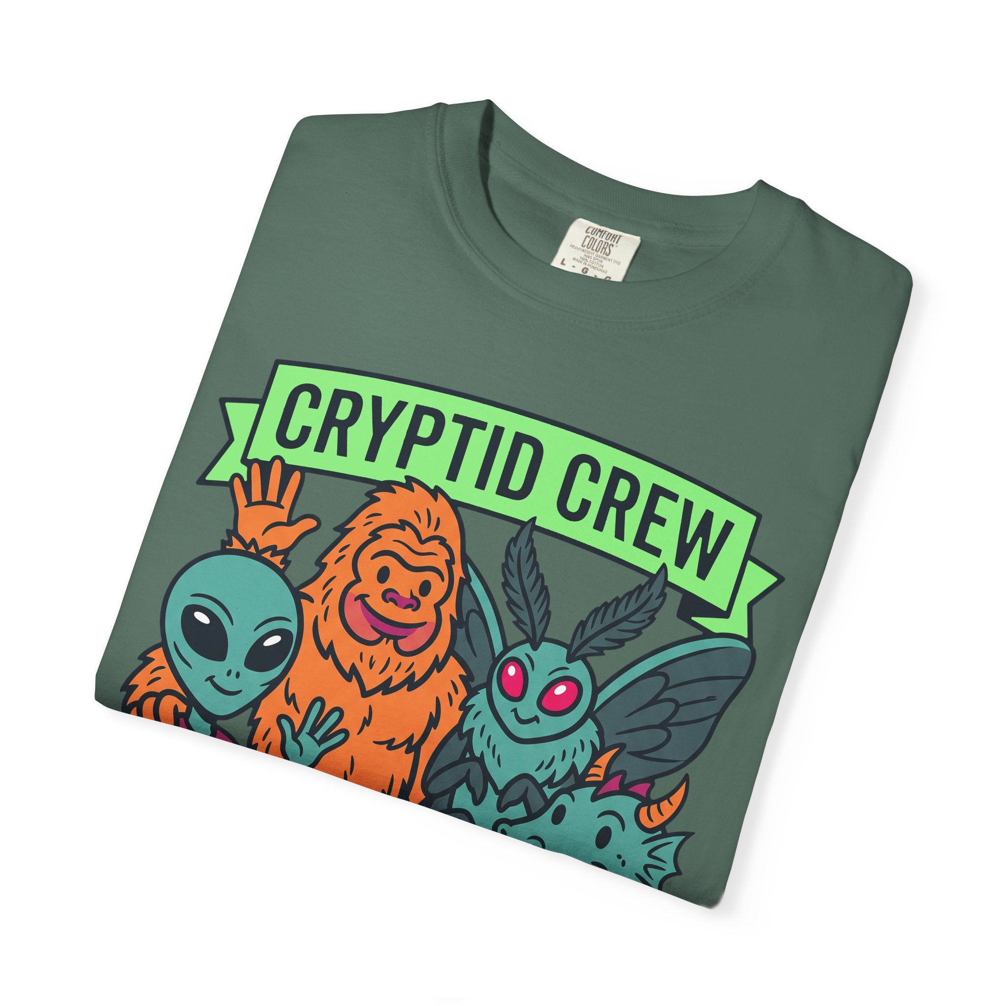 Sage green crew-neck T-shirt with 'CRYPTID CREW' graphic and monsters illustration.