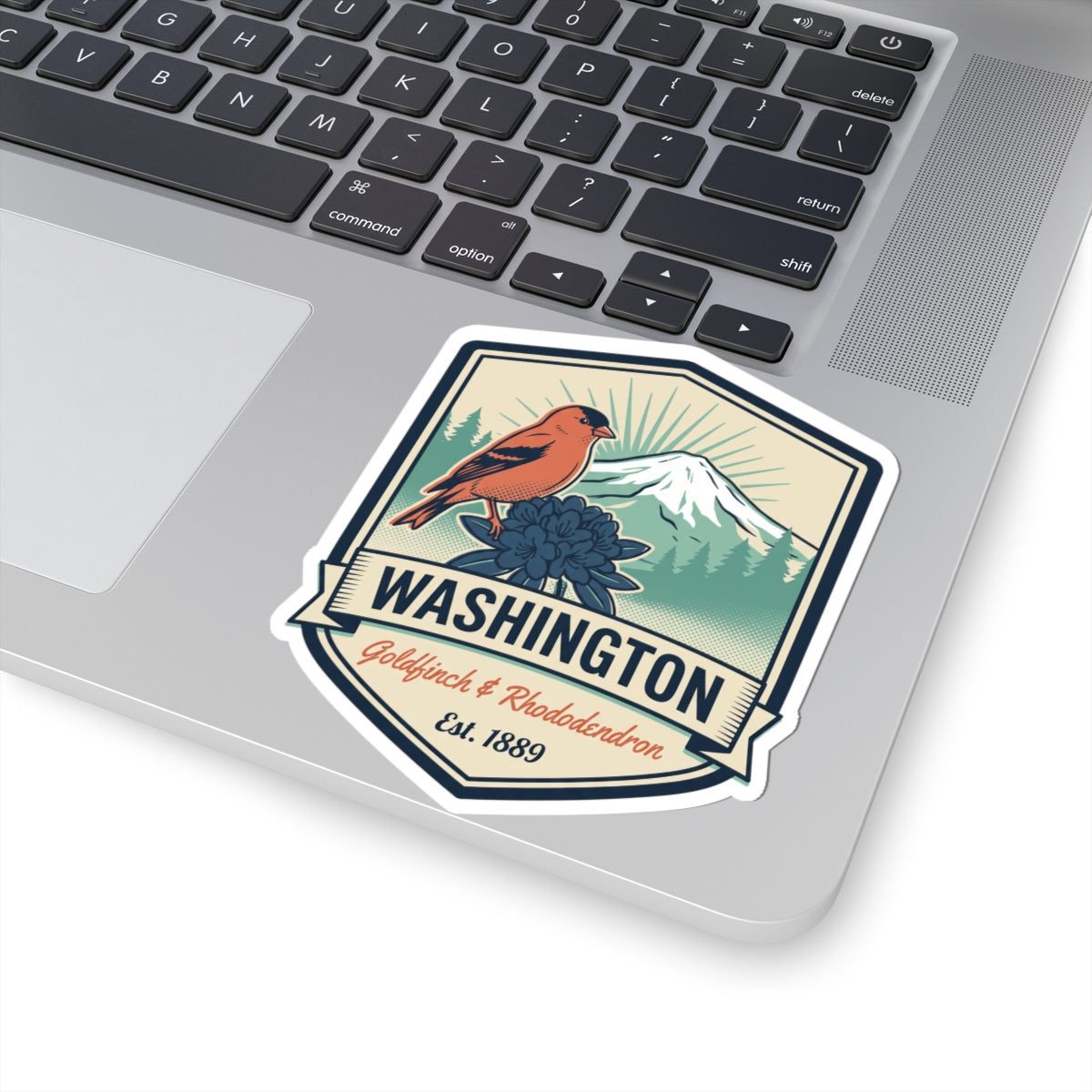 Washington badge sticker on laptop trackpad, orange bird over mountains and blue flower