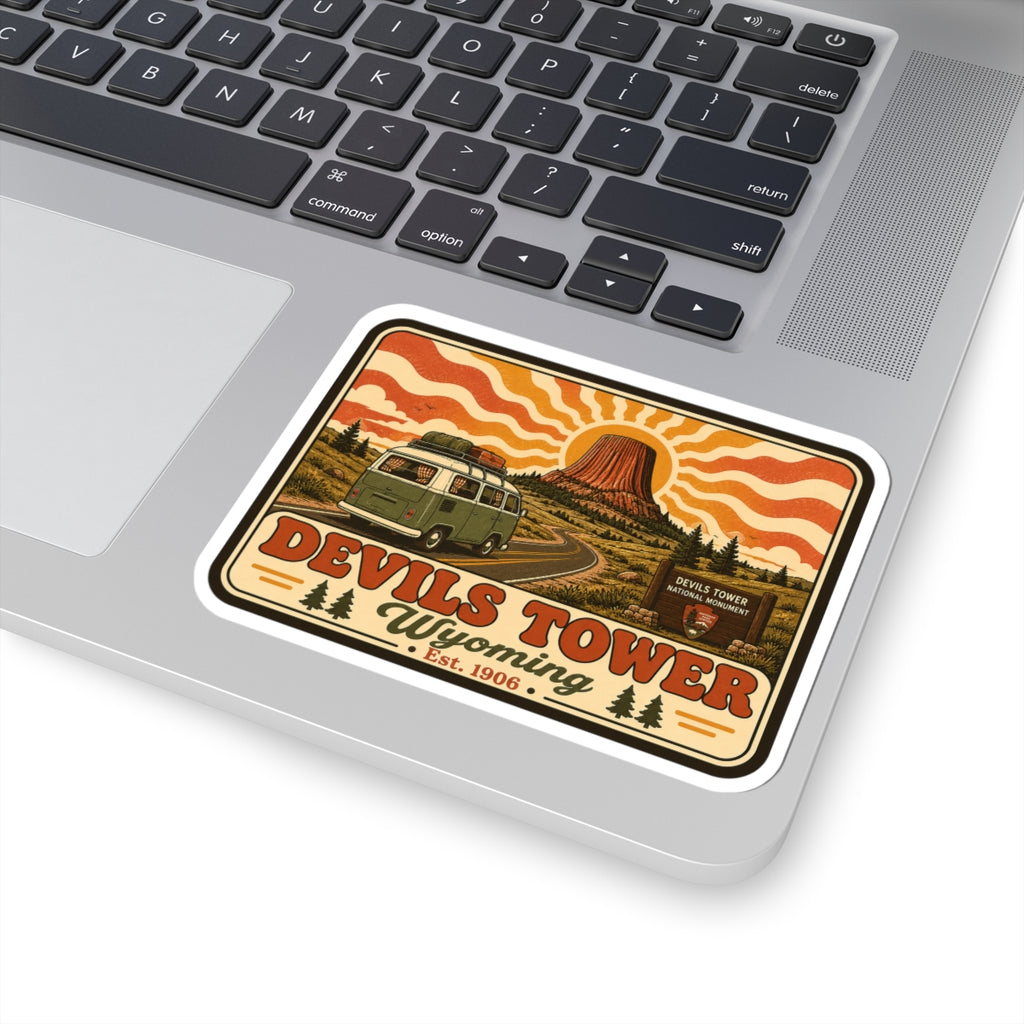 Kiss-cut sticker close-up: Devil’s Tower silhouette, green camper van, and orange wave background