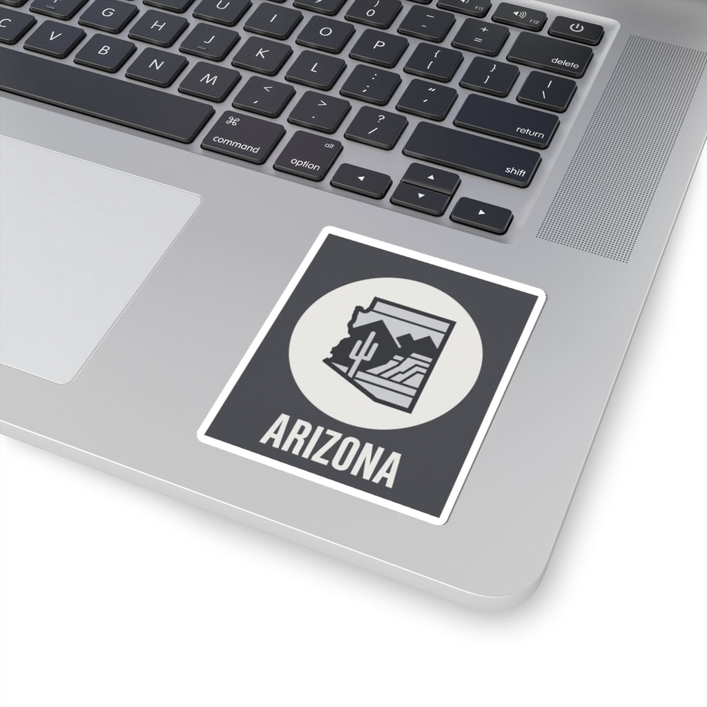 Arizona badge sticker on a laptop: dark square with white circle desert graphic and ARIZONA