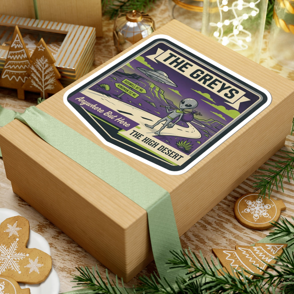 Die-cut sticker on gift box lid with gray alien and UFO over desert road scene.