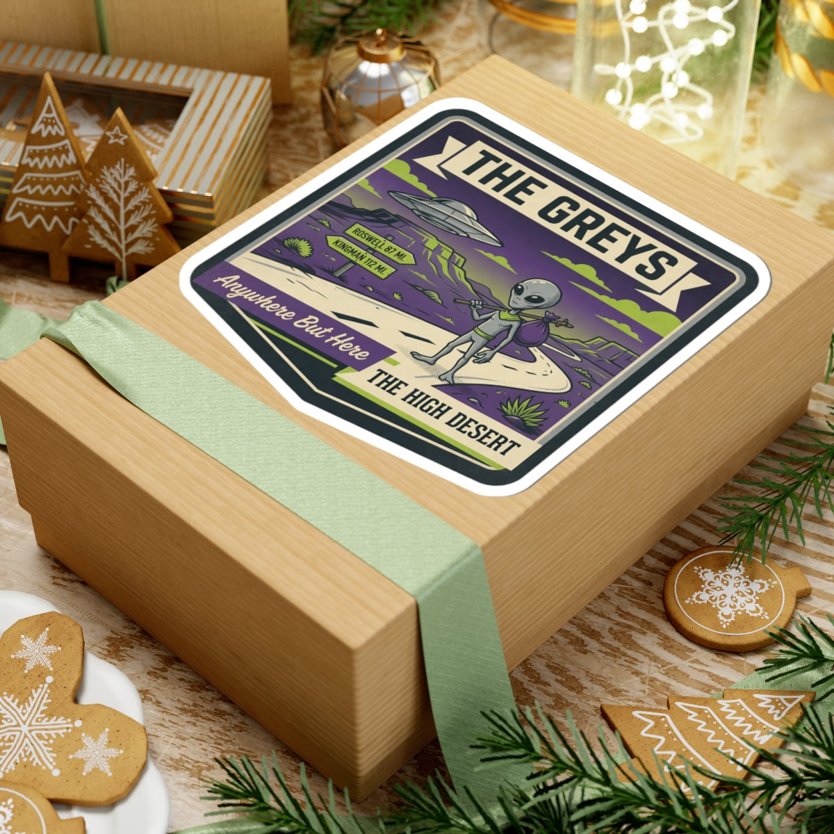 Die-cut sticker on gift box lid with gray alien and UFO over desert road scene.