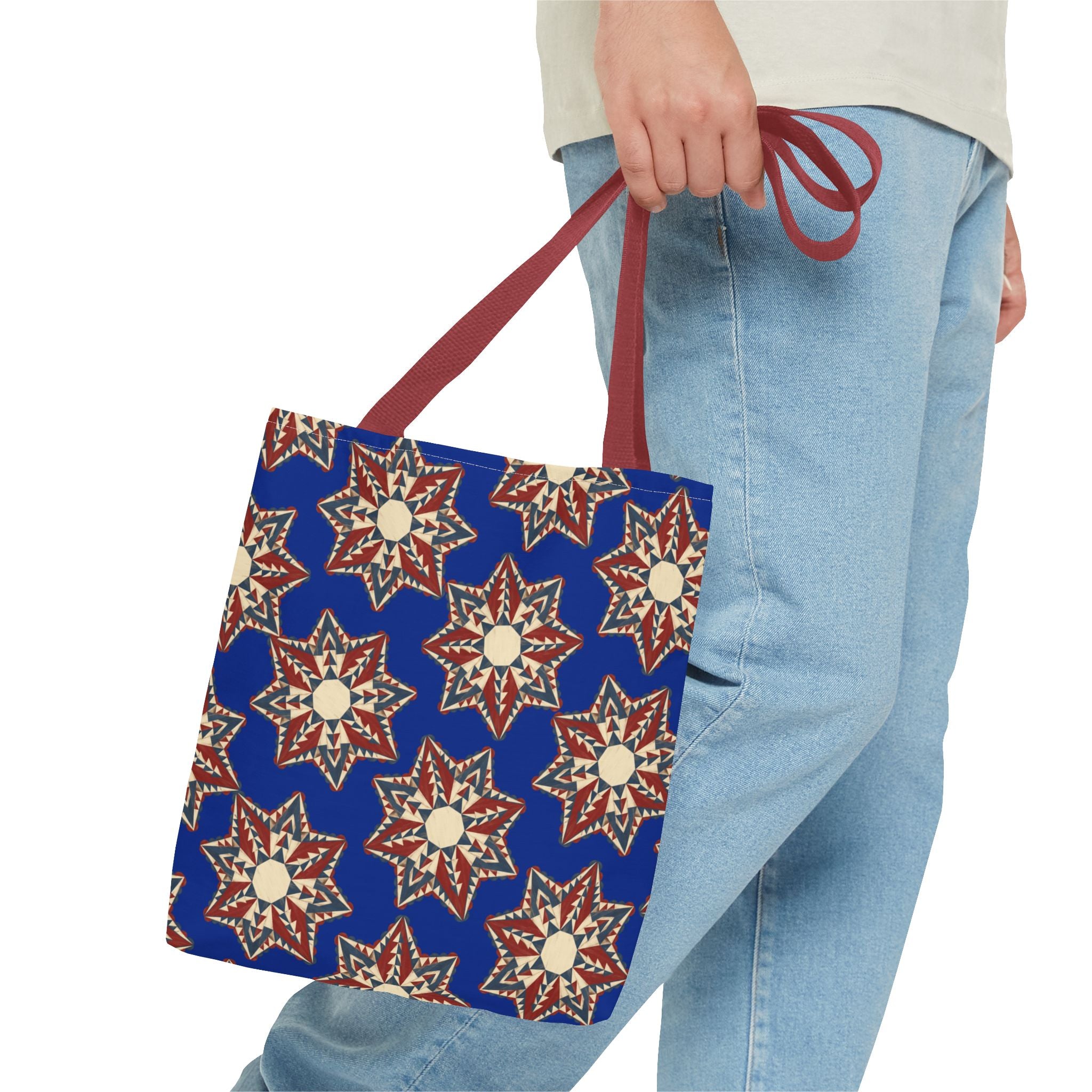 Blue tote bag with starburst floral pattern and red handles, held by hand