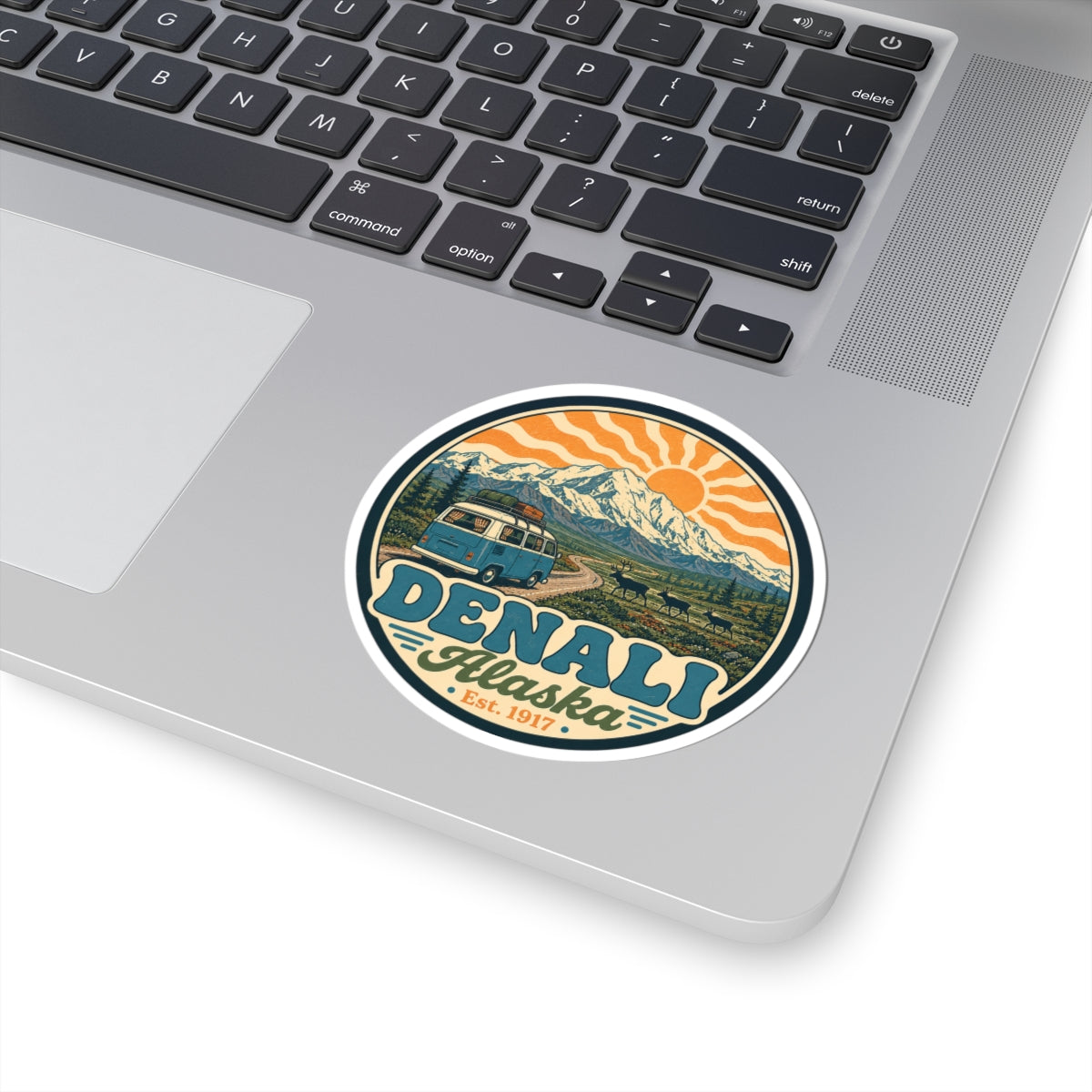 Denali Alaska circular sticker on a light laptop, with mountain, orange sun rays, teal van