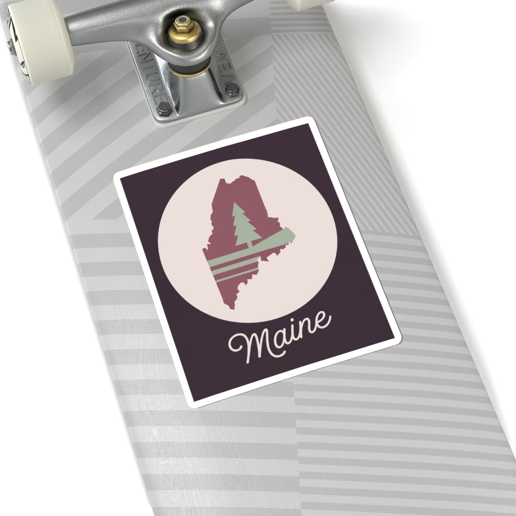 Maine silhouette vinyl decal on a suitcase, mauve state with pine tree and cursive 'Maine'.