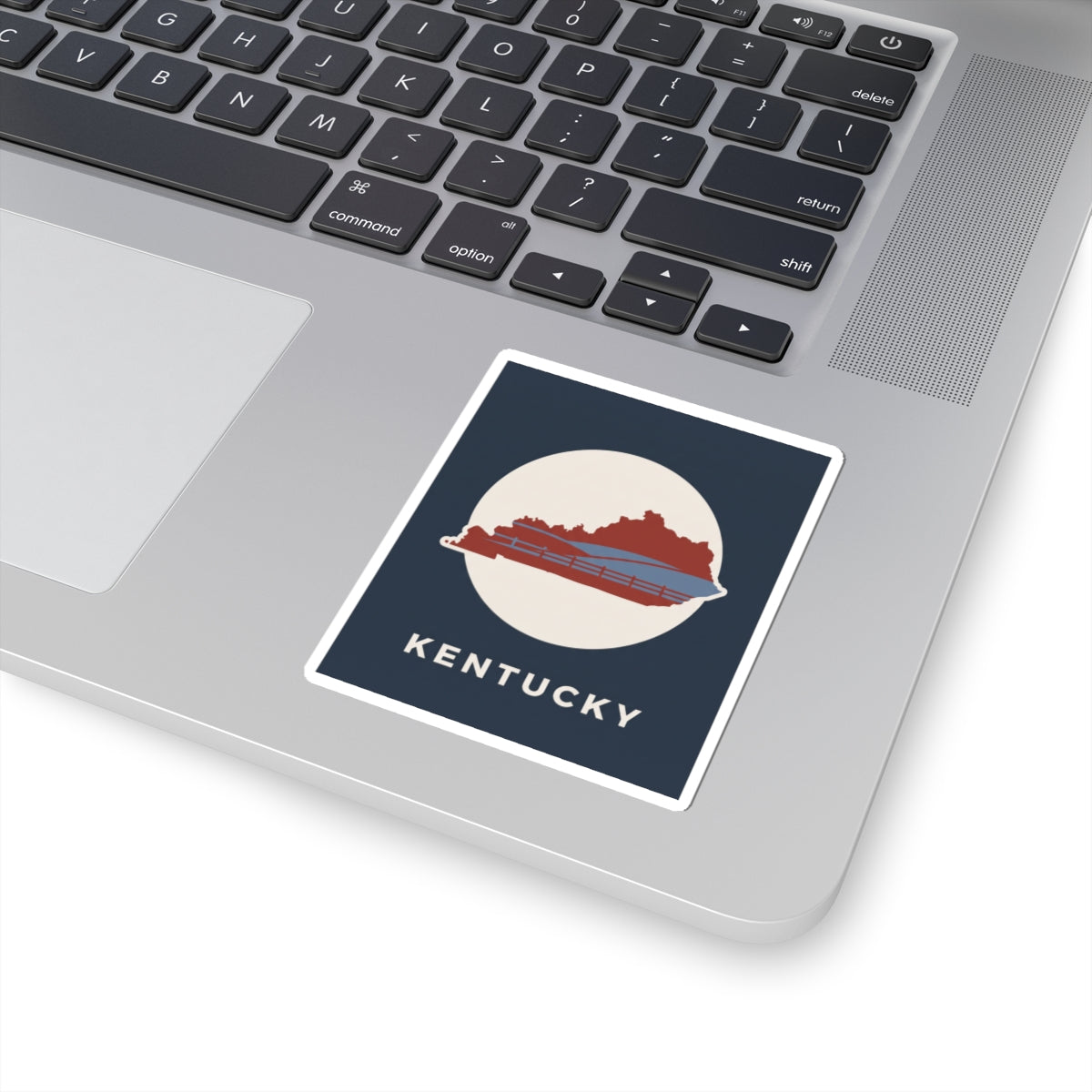Kentucky travel decal sticker on laptop keyboard: navy square with red state and bridge, KENTUCKY