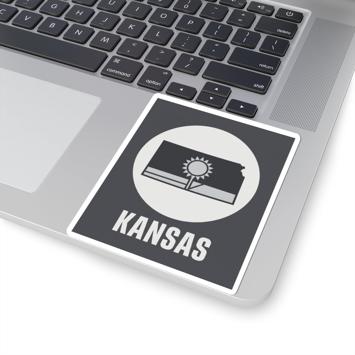 Kansas state sticker on a laptop trackpad area, dark gray square with sun and wheat field