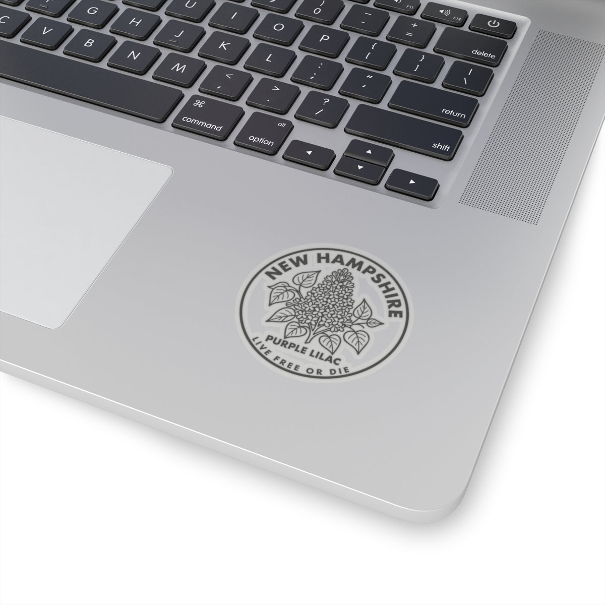 Round transparent-vinyl decal on a laptop lid, showing New Hampshire lilac logo
