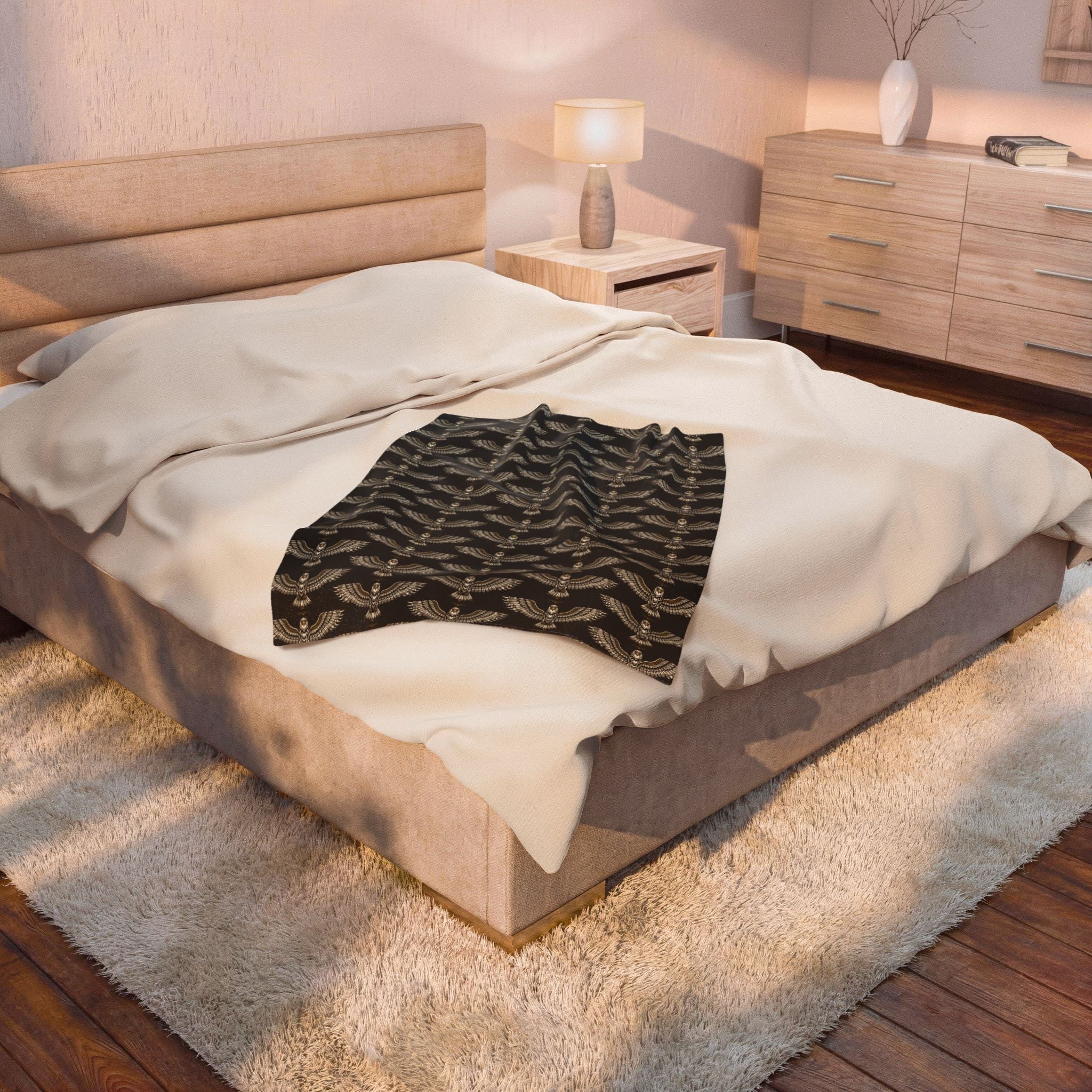 Winged skull patterned velveteen plush blanket, black with gold repeat, folded on bed