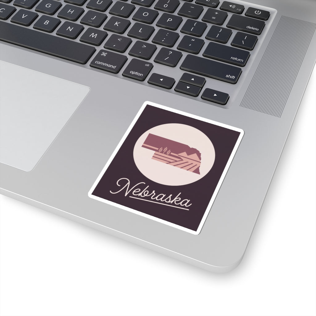Nebraska square kiss-cut decal on a laptop lid, circular farmland icon with cursive text