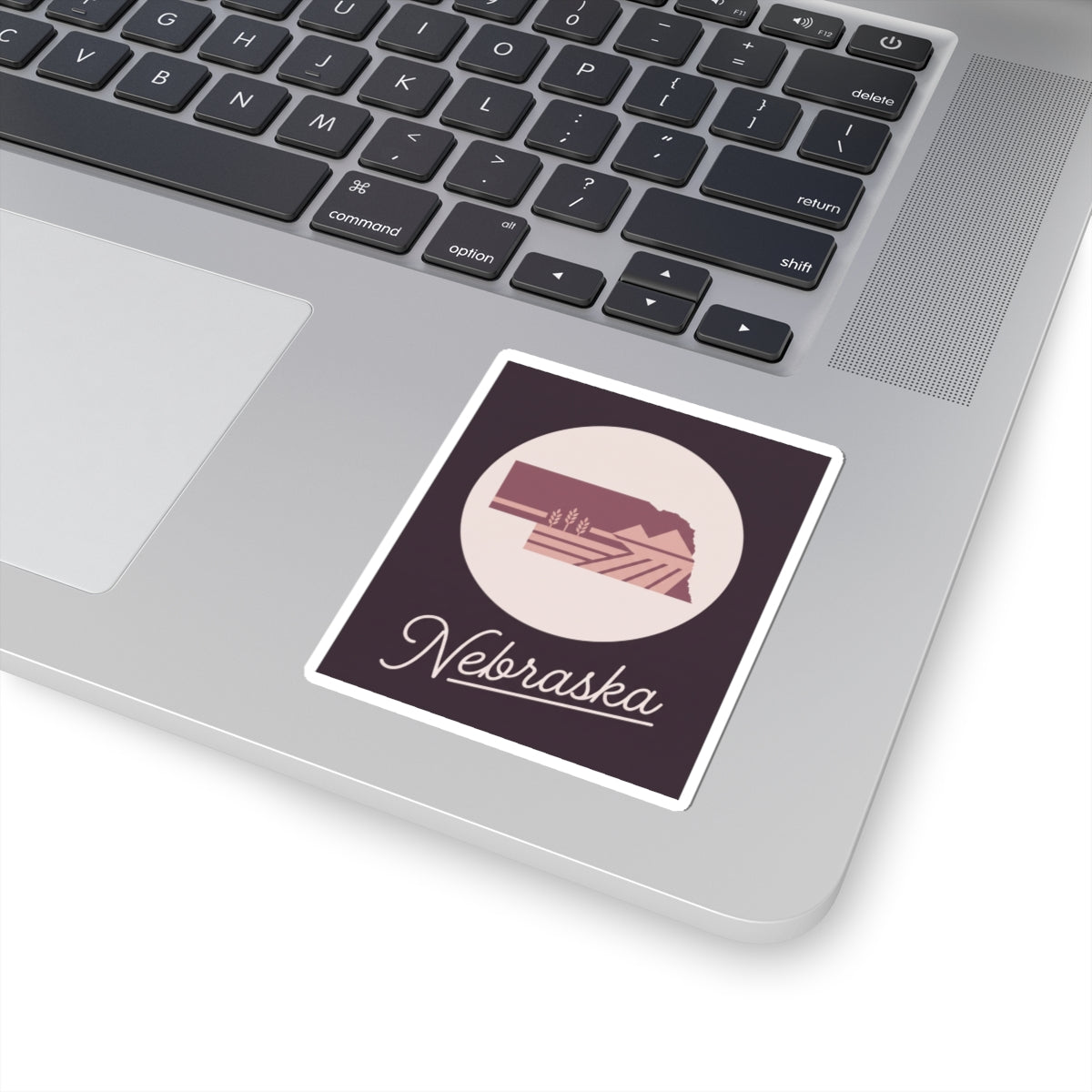 Nebraska square kiss-cut decal on a laptop lid, circular farmland icon with cursive text