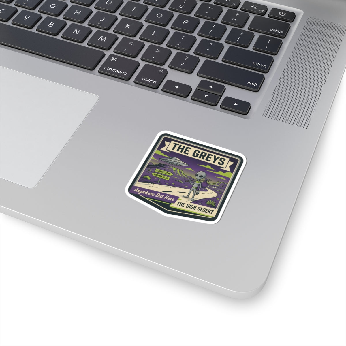 Square vinyl sticker with alien and UFO art and bold text, on a laptop lid