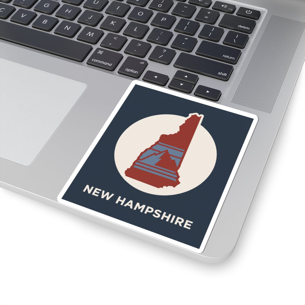 New Hampshire state silhouette sticker on laptop palm rest: navy panel with red NH in white circle
