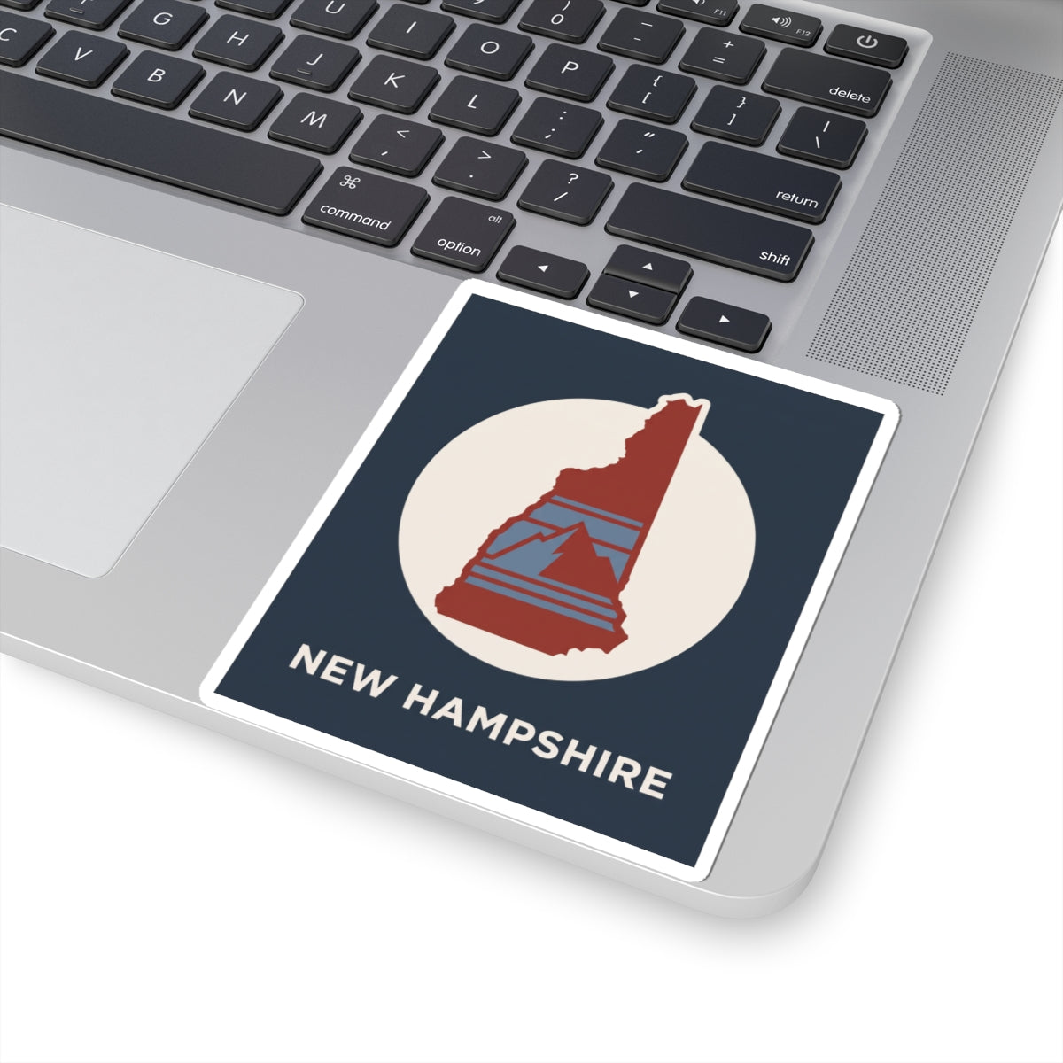 New Hampshire state silhouette sticker on laptop palm rest: navy panel with red NH in white circle