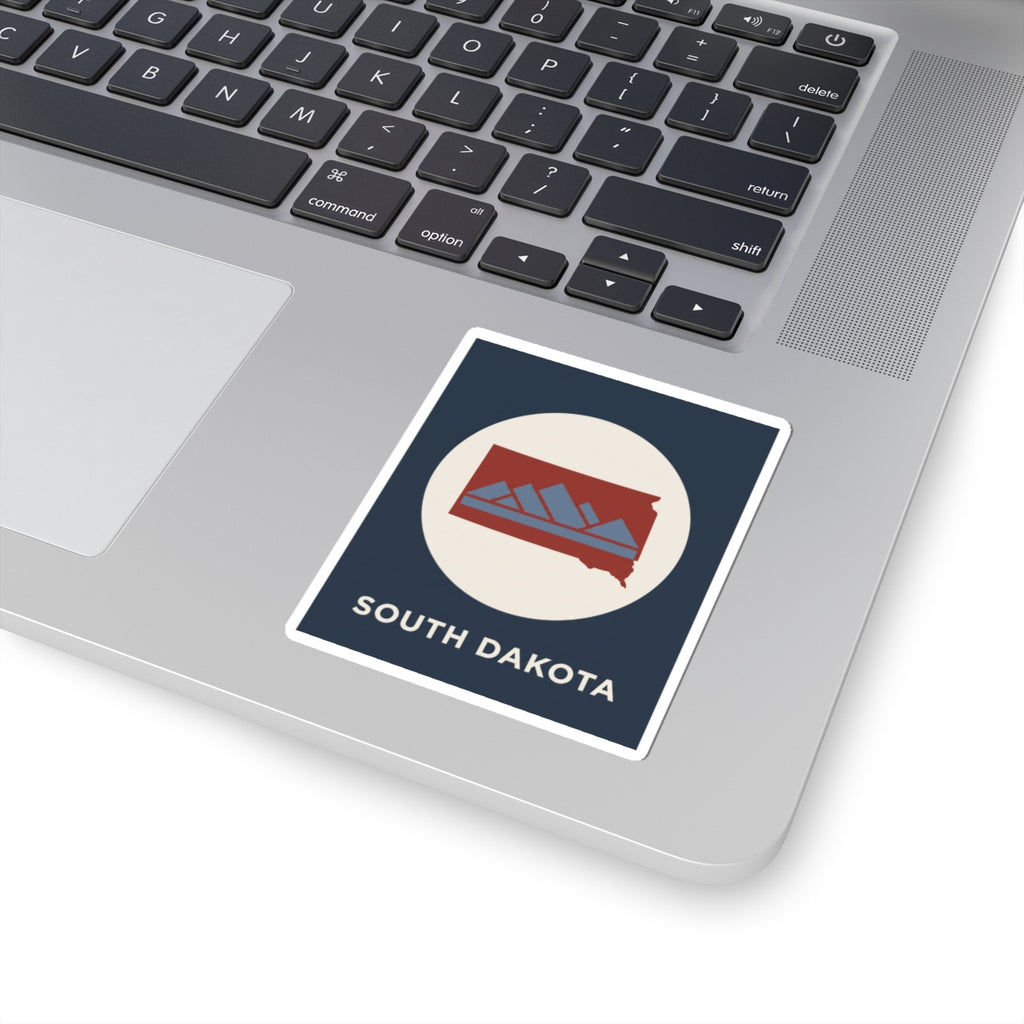 South Dakota map badge sticker placed on a laptop keyboard with navy square and white circle design