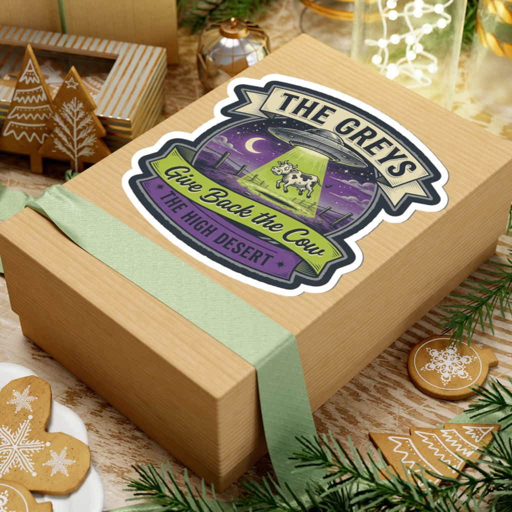 Die-cut sticker on a wrapped gift box with teal ribbon, featuring 'THE GREYS' and 'Give Back the Cow'.