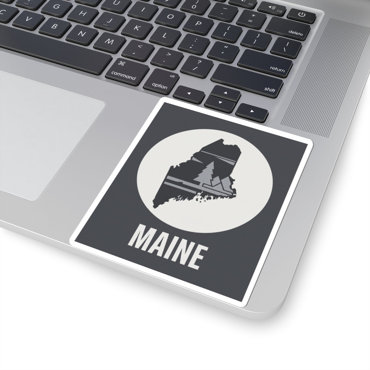 Rectangular Maine sticker with circular cream emblem, pine tree map and 'MAINE' lettering.