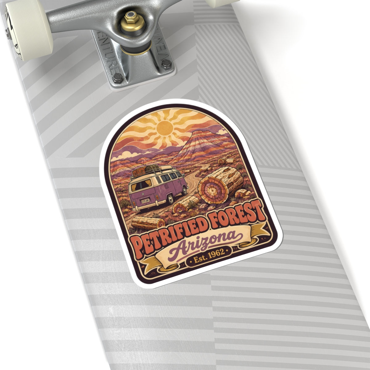 Kiss-cut sticker on skateboard deck with purple camper van, sun and logs, 'Petrified Forest Arizona Est. 1962'.