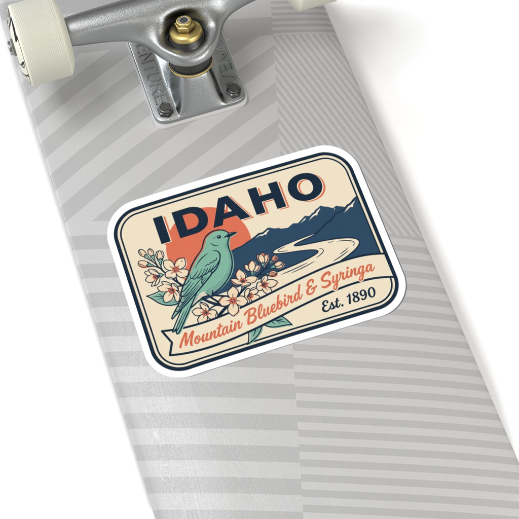 Rounded vinyl sticker: IDAHO over mountains with bluebird, blossoms, and Est. 1890