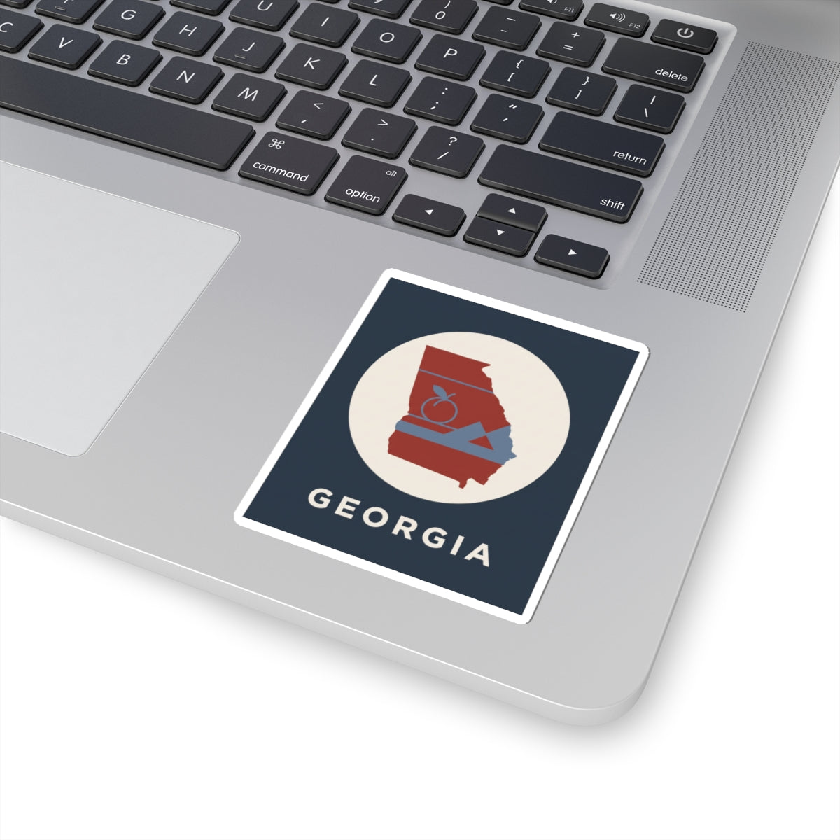 Georgia outline sticker on laptop: circular red state design with peach icon, mountains, “GEORGIA”