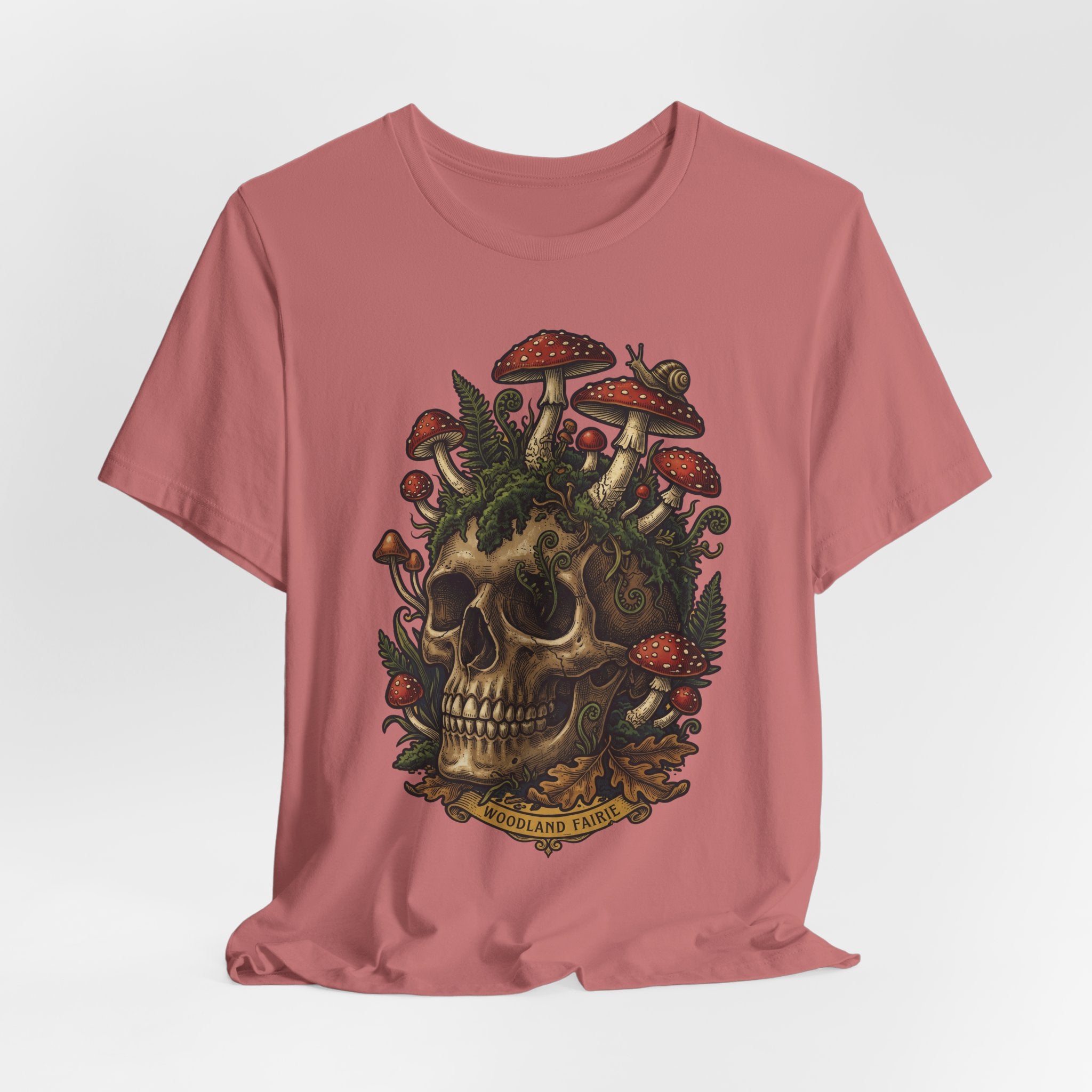 Mushroom skull T-shirt rosa: calavera con setas rojas y vegetación tipo bosque.