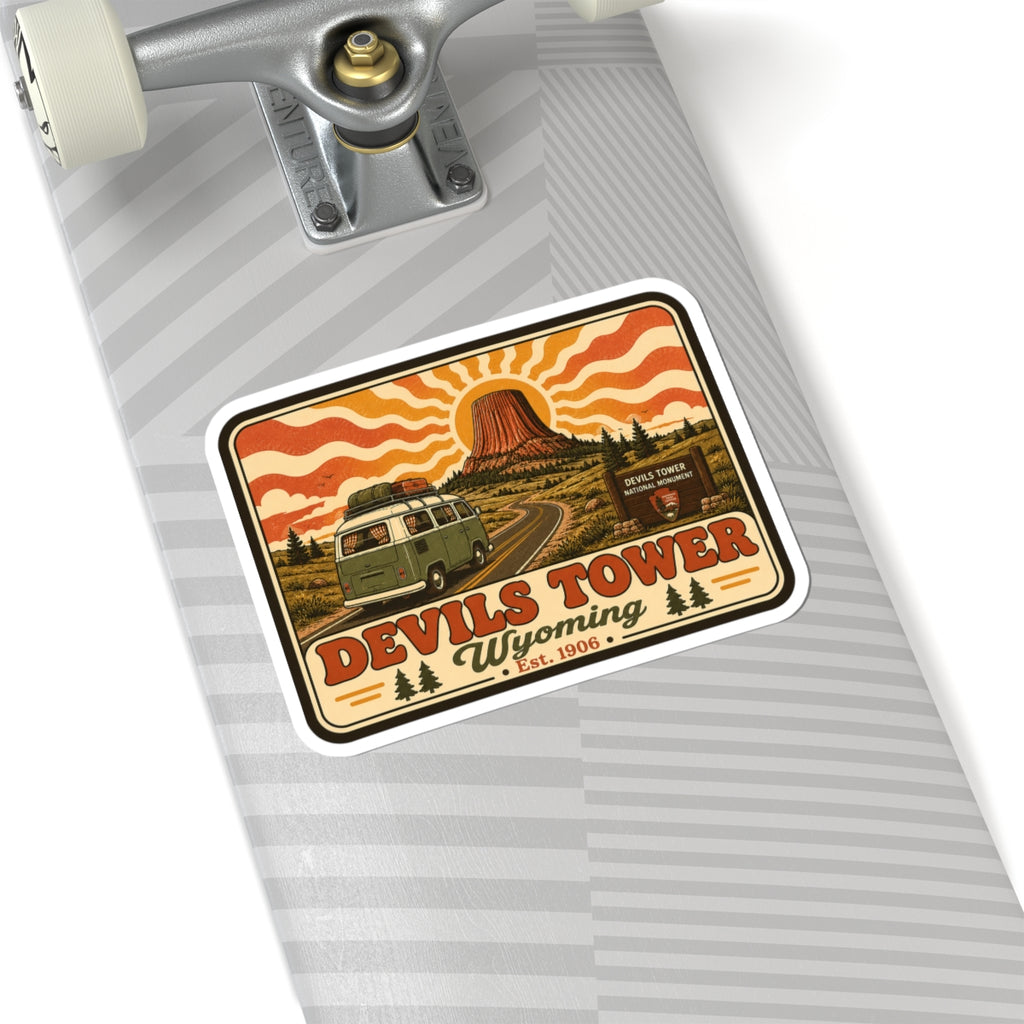 Kiss-cut sticker with Devil’s Tower rock, green camper, and “Wyoming” text under orange waves