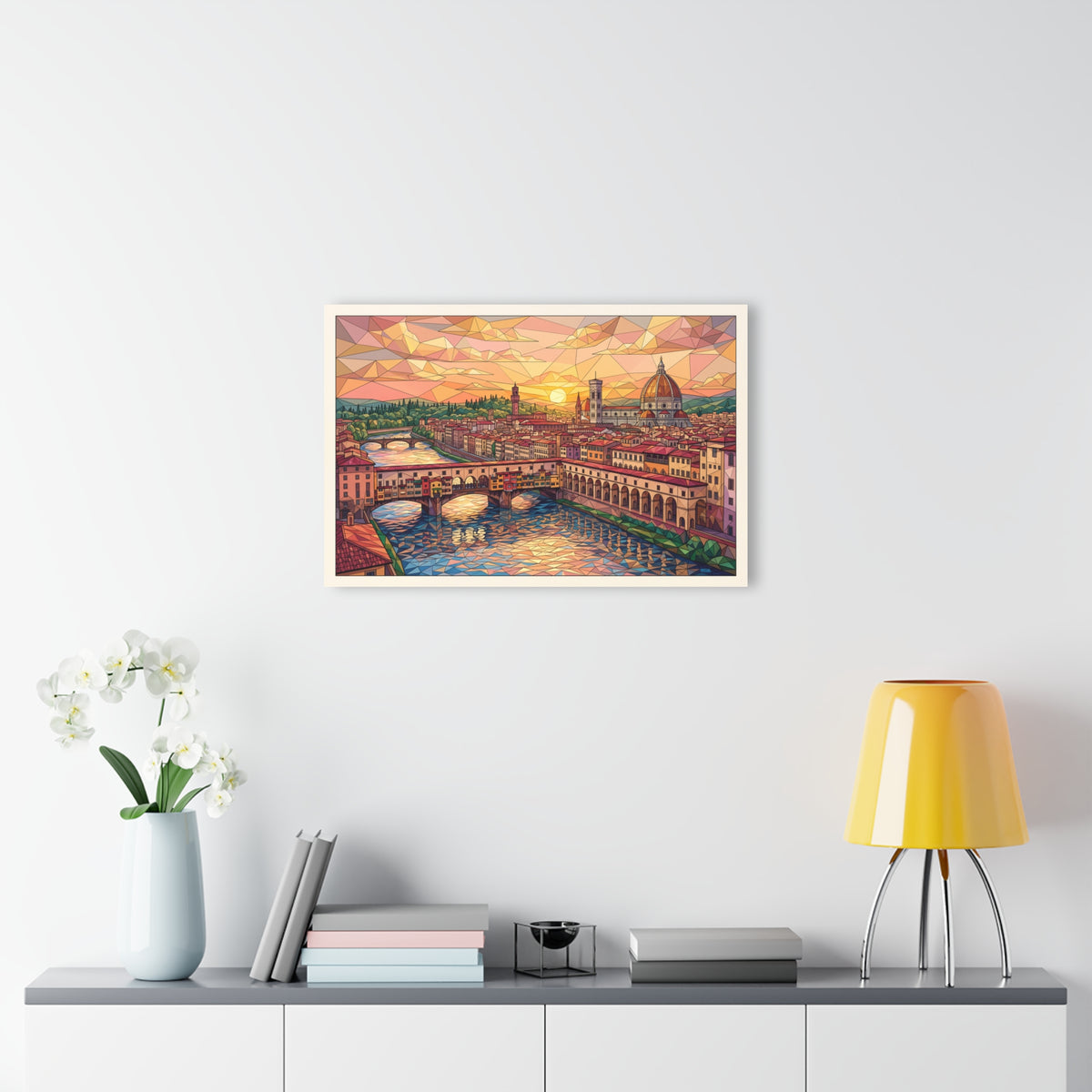Framed acrylic cityscape wall art above console with books, vase, and yellow lamp