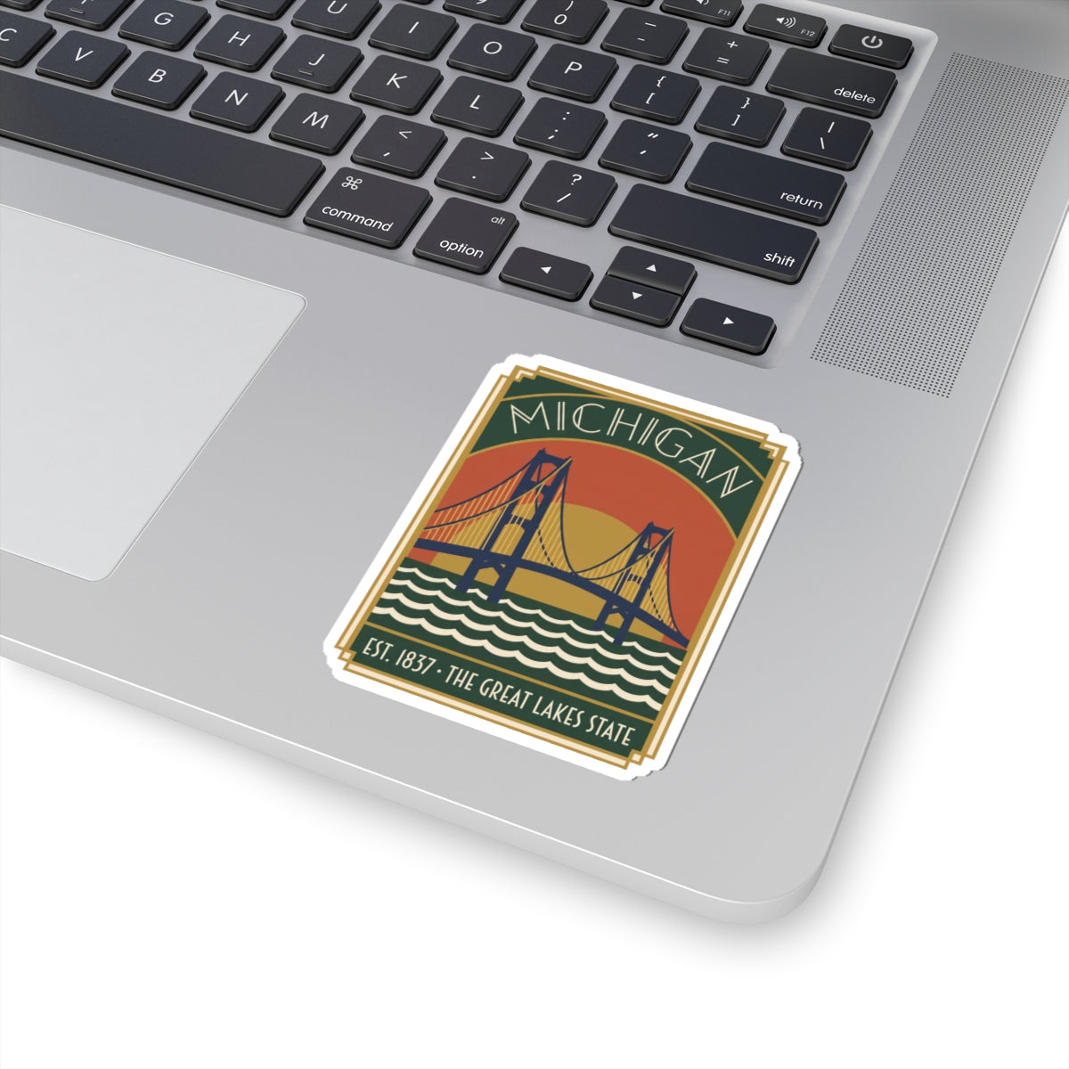 Michigan bridge die-cut sticker on a laptop keyboard, green banner and blue wave design