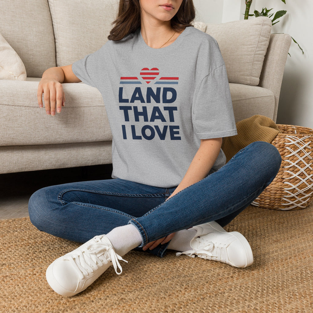 Gray T-shirt with “LAND THAT I LOVE” graphic, red heart above blue stripes, crew neck.