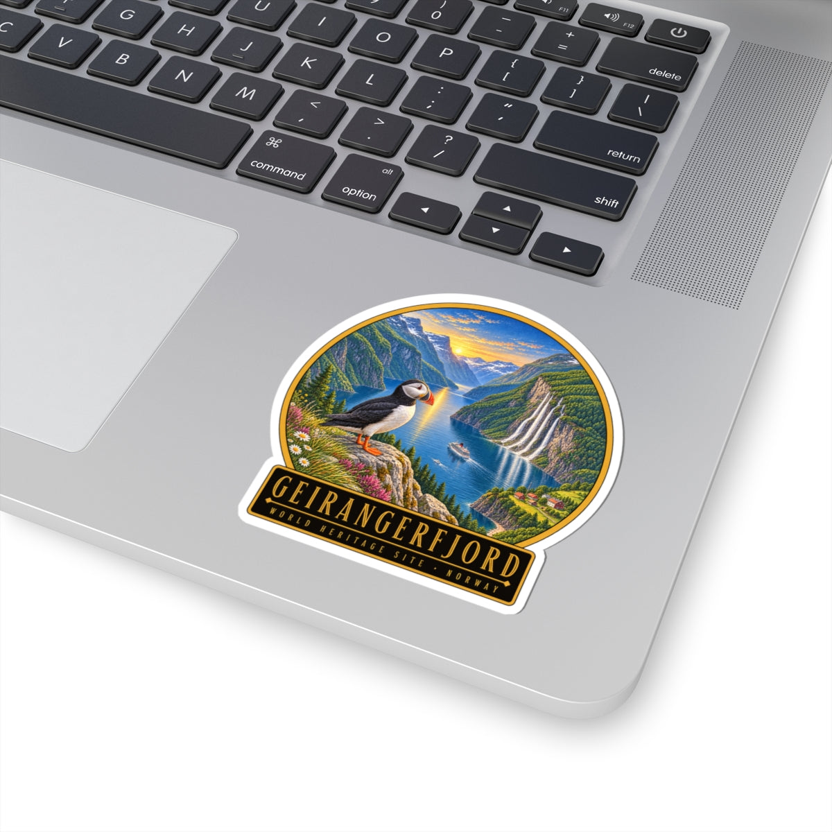 Geirangerfjord sticker on a laptop keyboard: puffin over fjord with “GEIRANGERFJORD” text