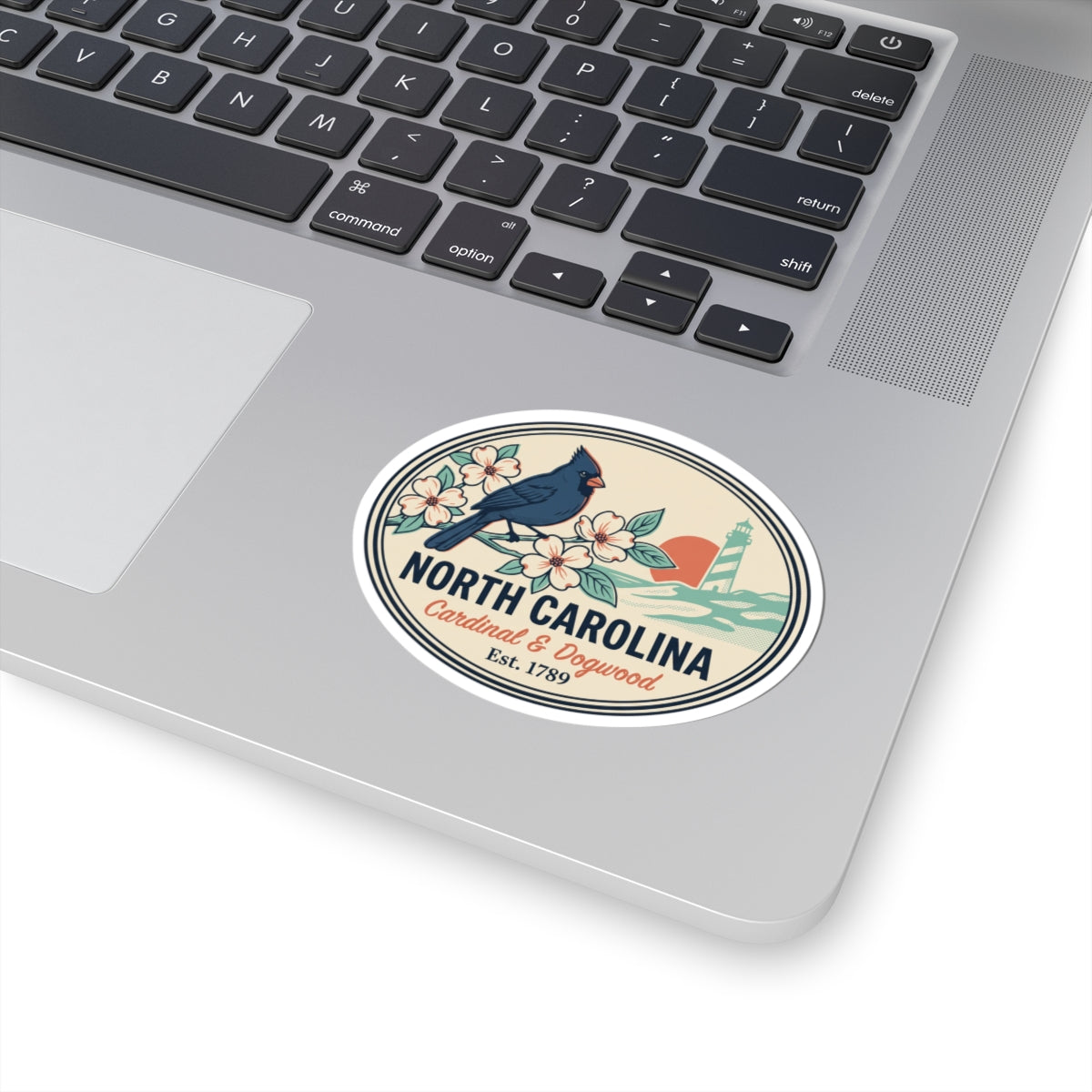 North Carolina state badge sticker on a laptop surface, with cardinal, flowers, and lighthouse