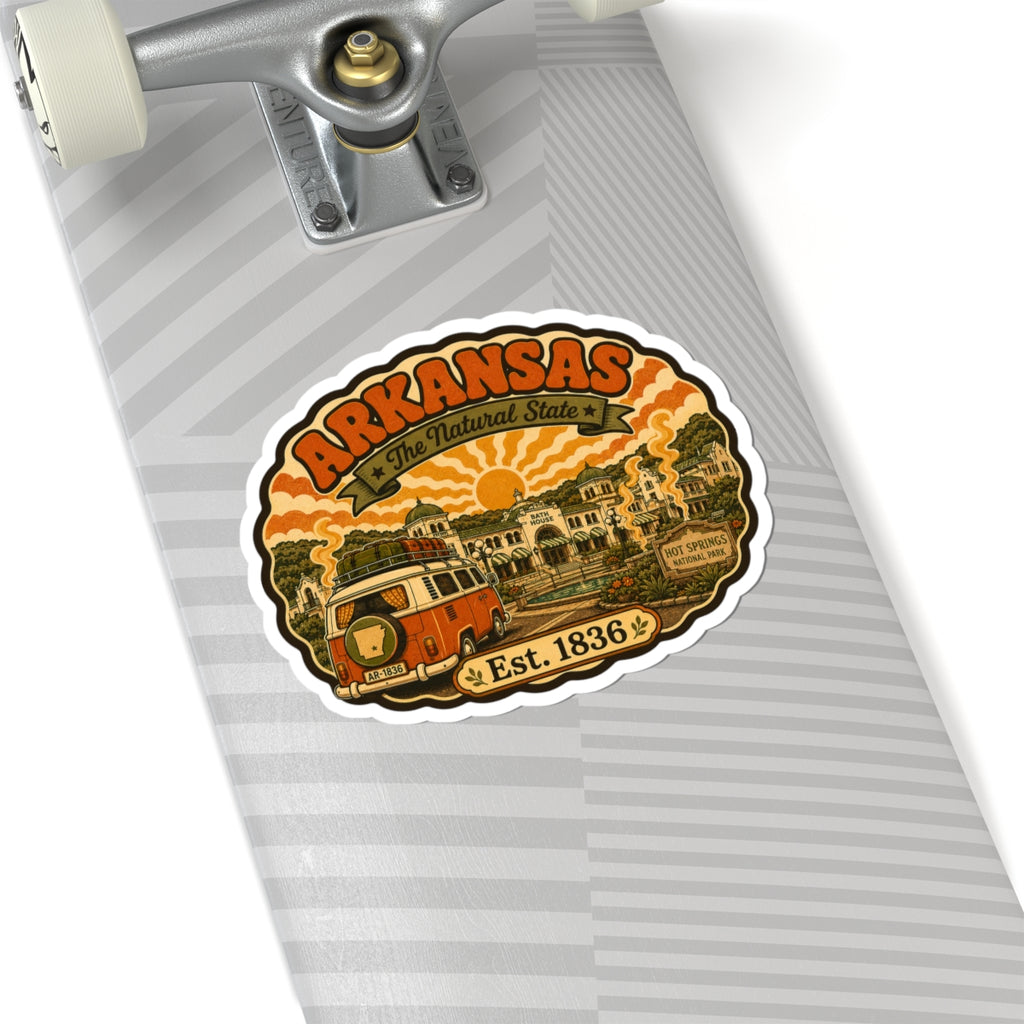 Round Arkansas travel sticker with orange camper van and “Est. 1836” on gray surface