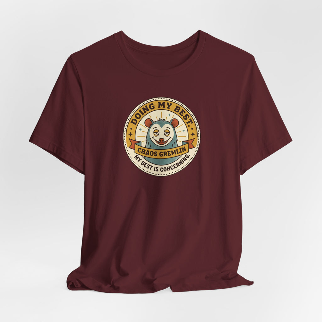 Maroon crew-neck T-shirt with centered circular gremlin badge graphic.