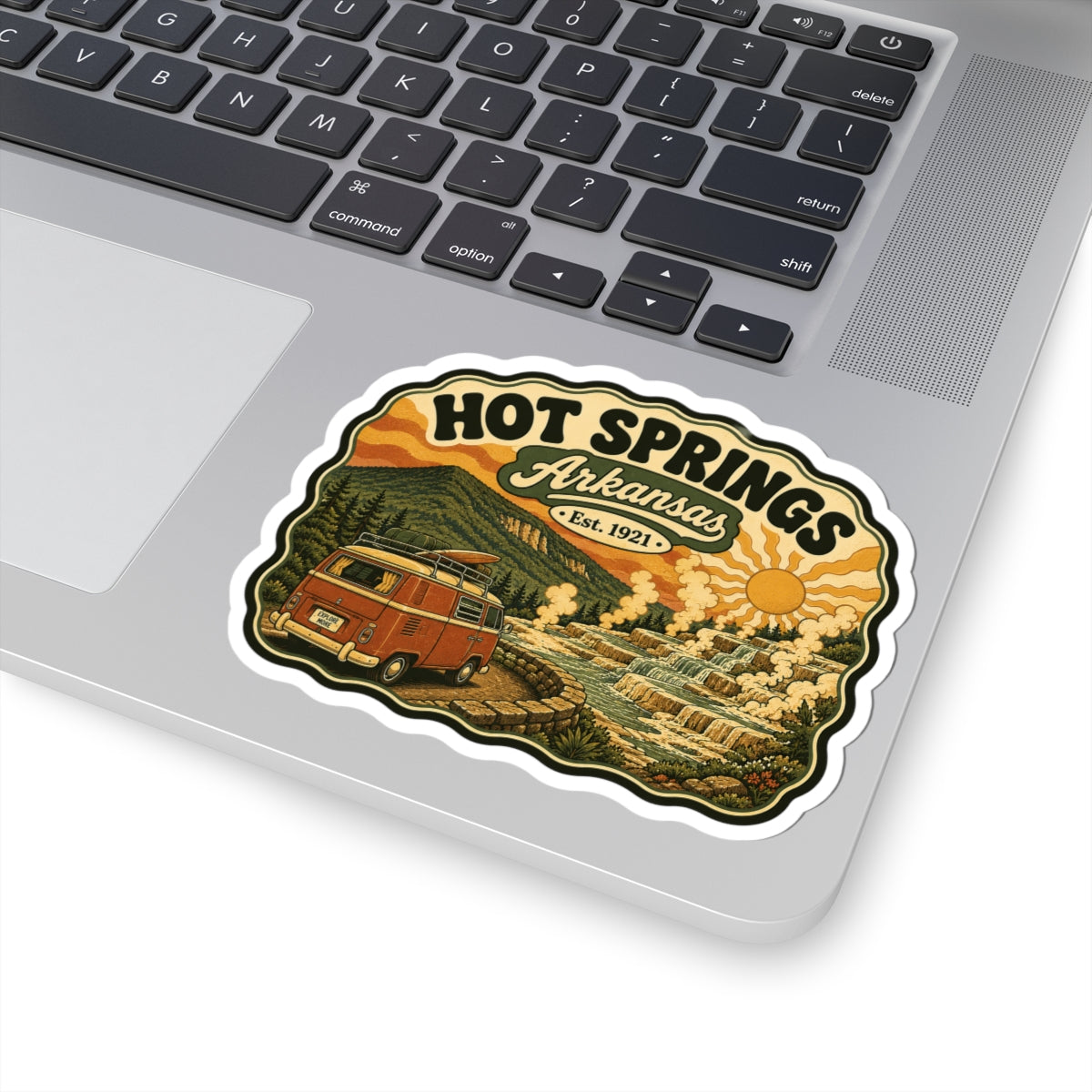 Die-cut Hot Springs Arkansas sticker on laptop lid with vintage camper van, hot springs, and sun