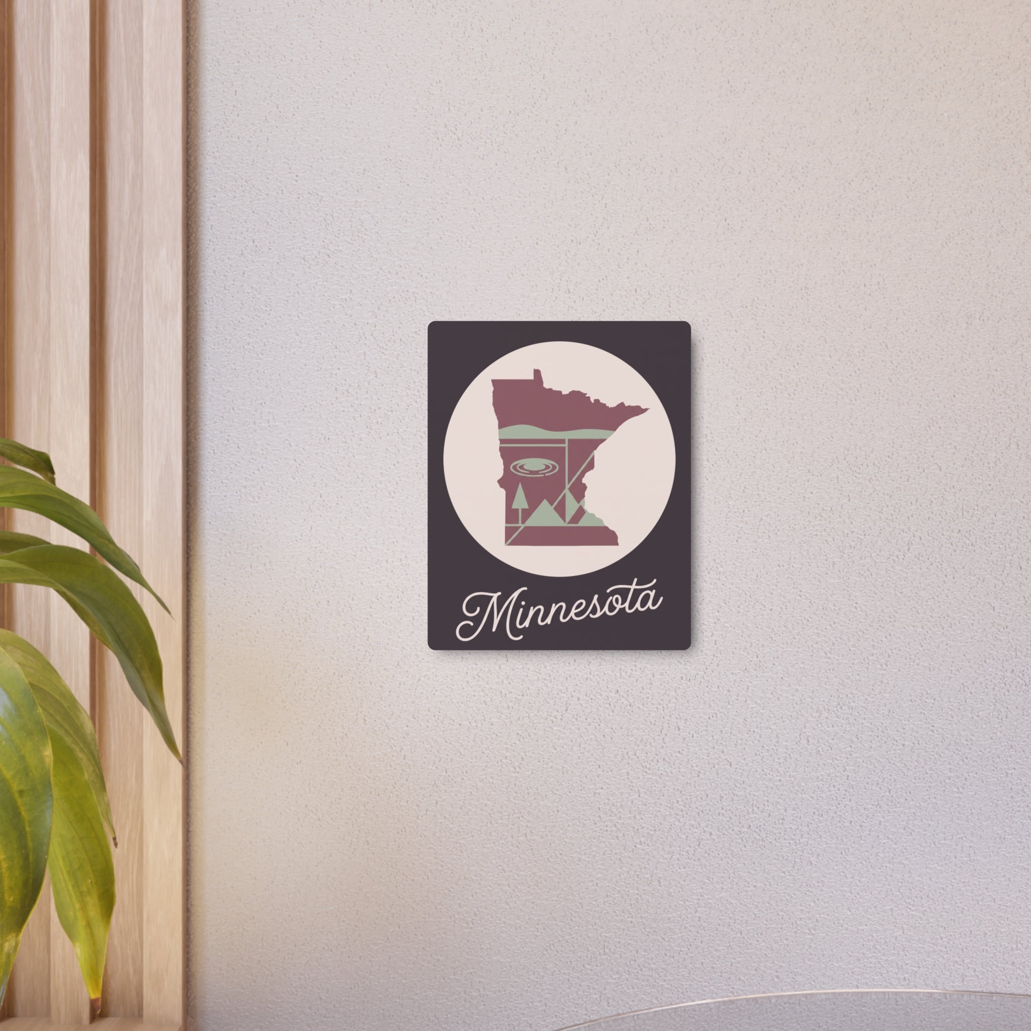 Small Minnesota metal wall art sign on wall with dark square, circular silhouette, pink-and-sage “Minnesota” script.