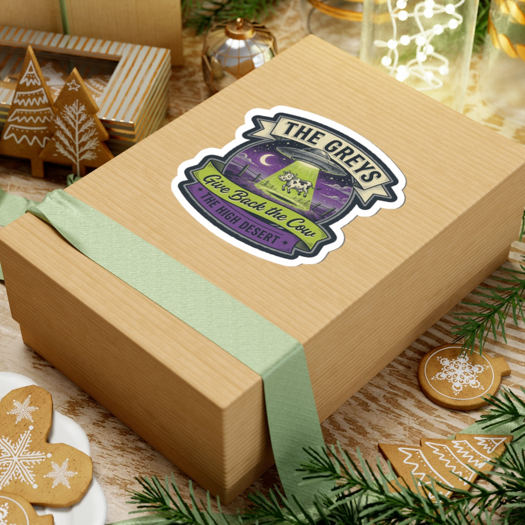 Die-cut sticker on a kraft gift with teal ribbon, text 'THE GREYS' and 'Give Back the Cow'.