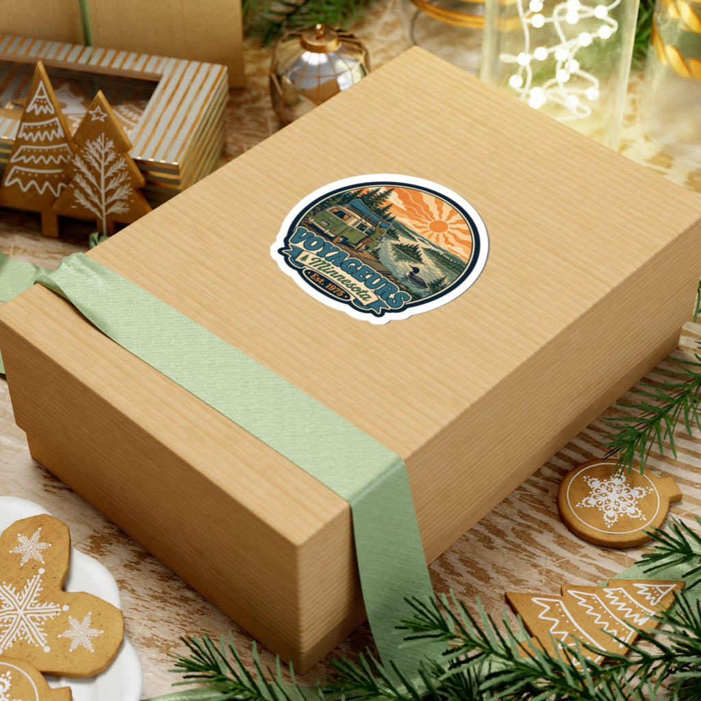 Round die-cut sticker: green camper van, pine forest, lake shore and orange sun; Voyageurs Minnesota