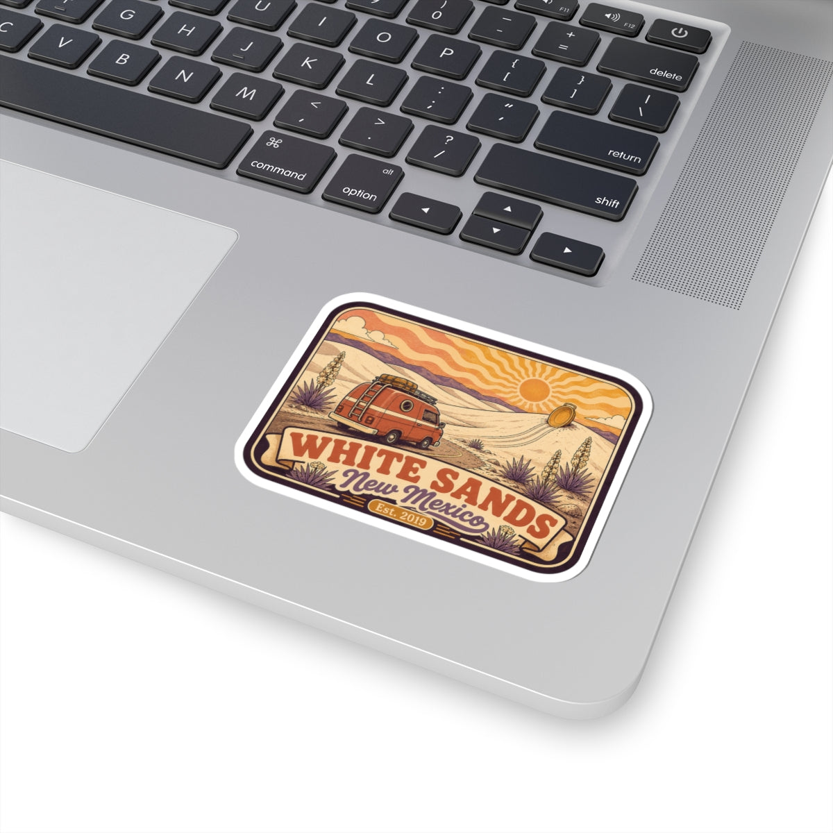 White Sands kiss-cut vinyl sticker on a laptop corner, with retro van, desert dunes, and “White Sands” text