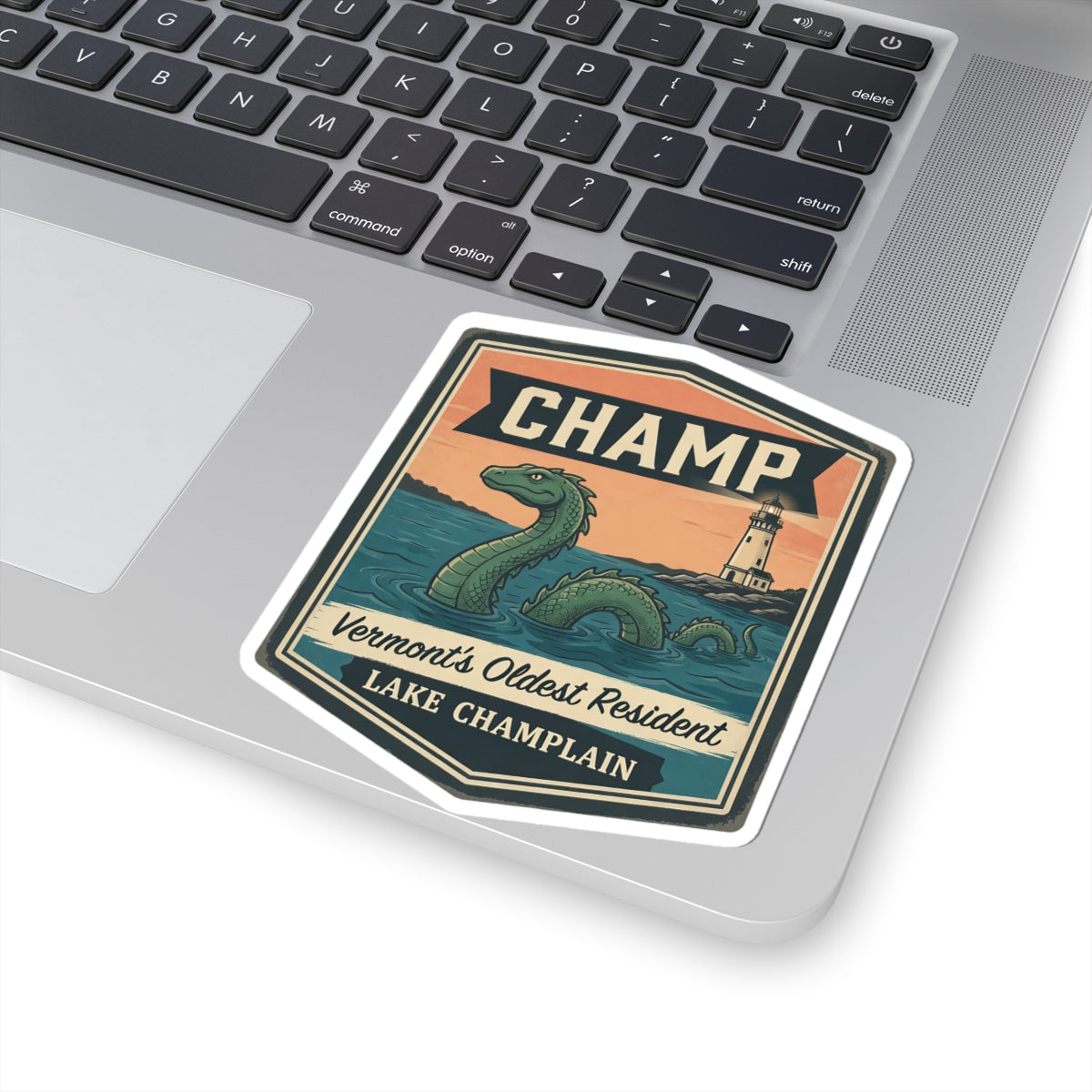 Laptop sticker with CHAMP lettering and green sea serpent, lighthouse, and lake text