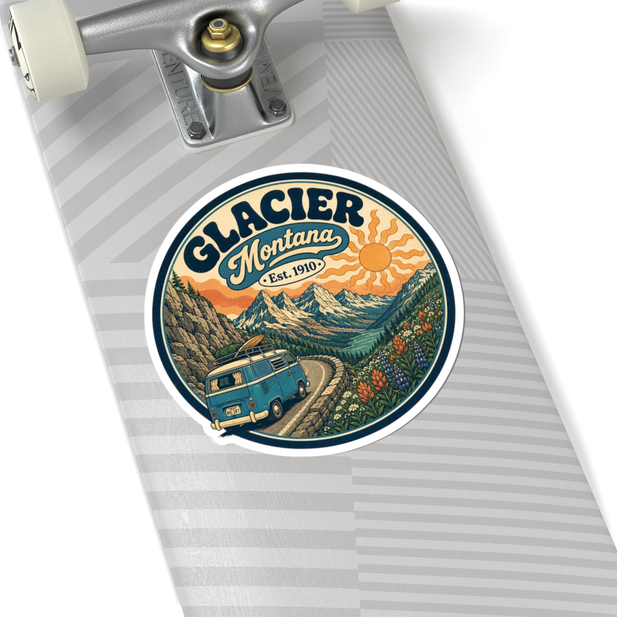 Round kiss-cut sticker with Glacier Montana text, orange sun, mountain peaks, and teal camper van