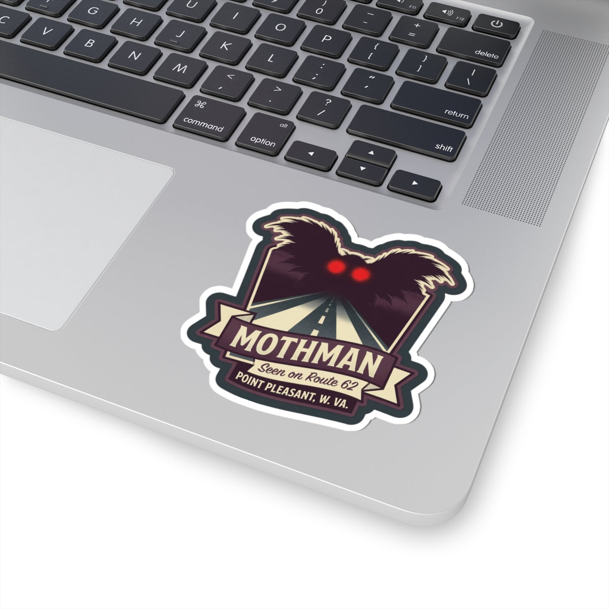 Kiss-cut Mothman sticker on a laptop lid, with red eyes and Route 62 road artwork