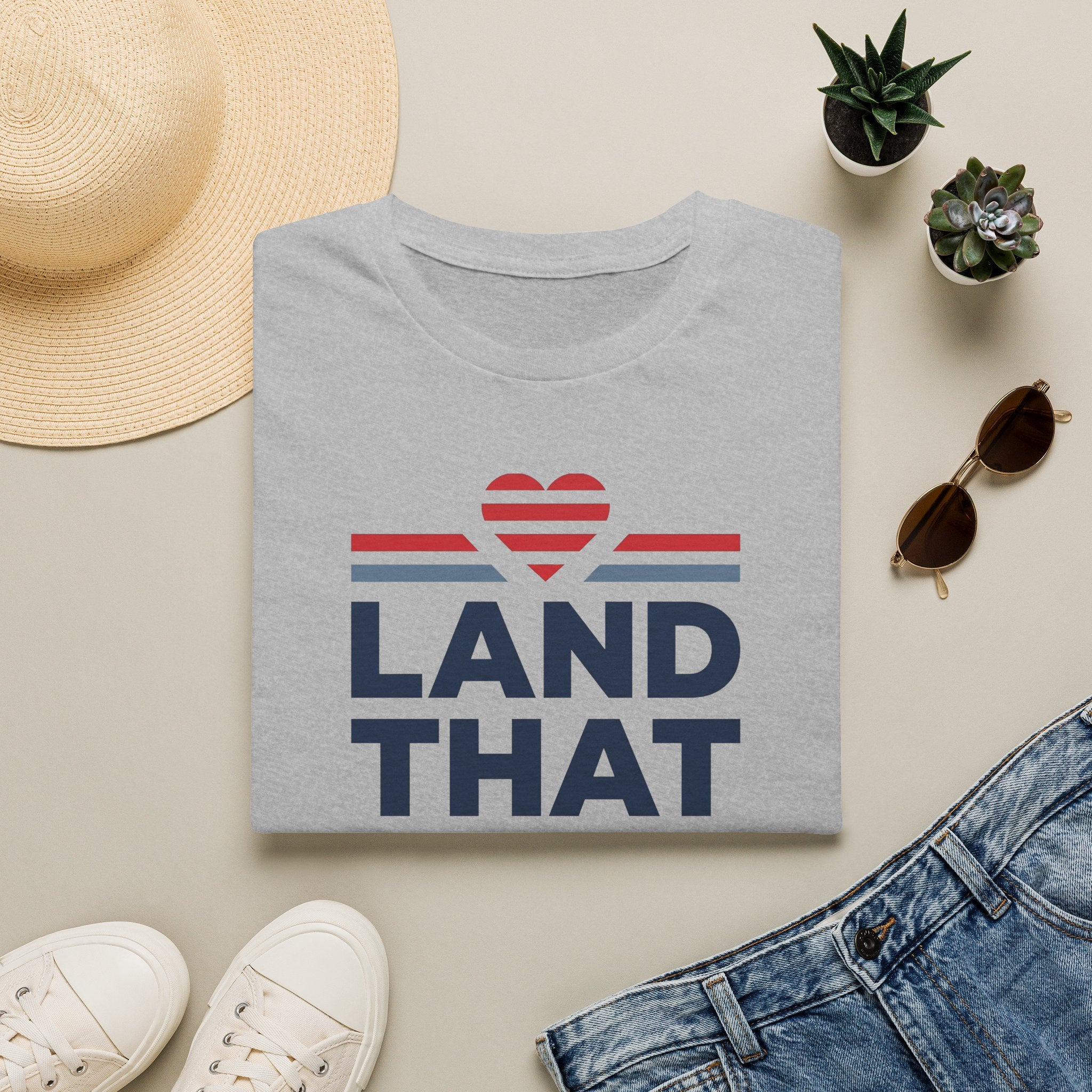 Gray T-shirt with “LAND THAT” graphic and red heart above blue stripes, crew neck.
